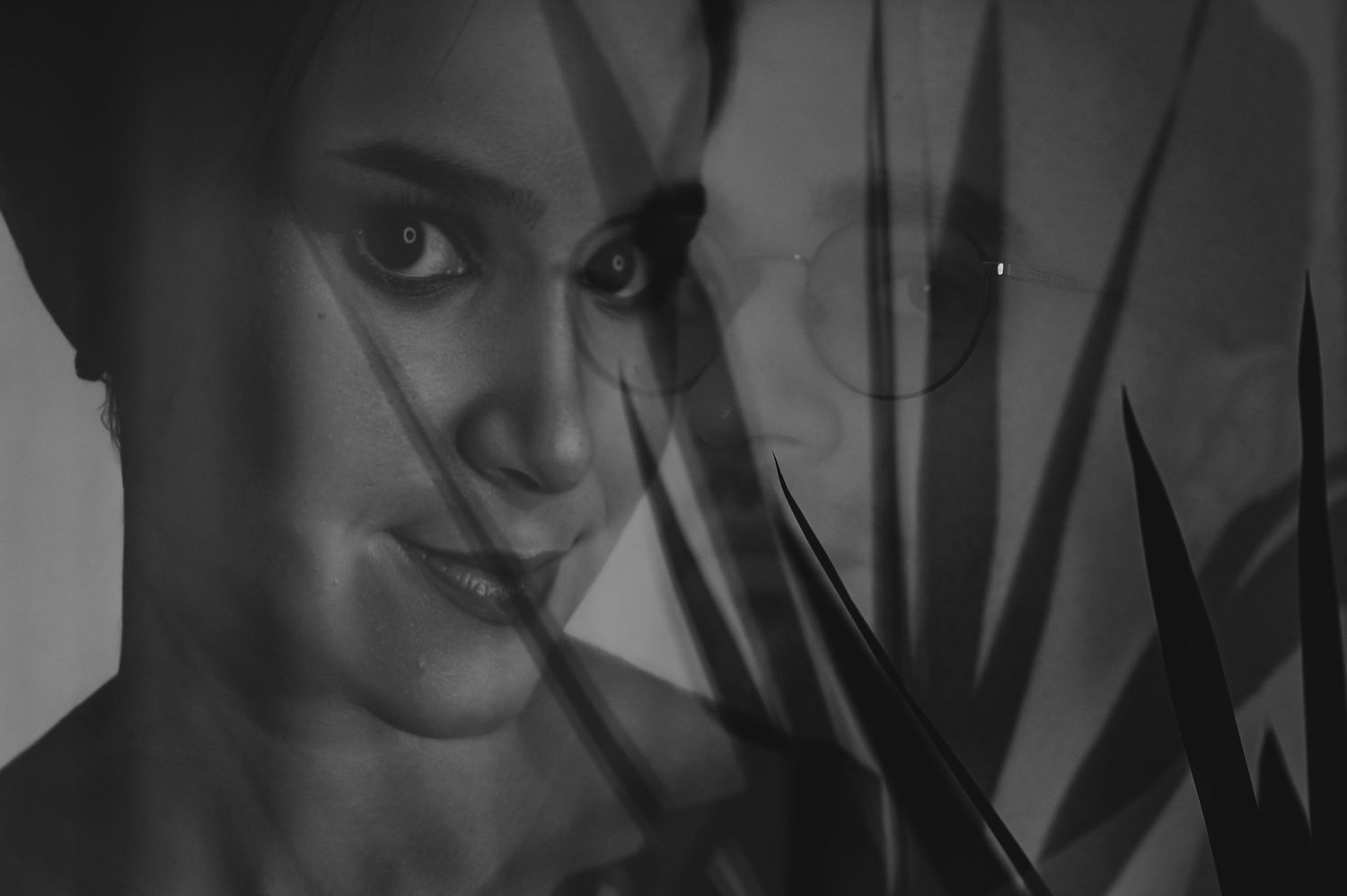 Black and white portrait of a woman smiling through bamboo leaves, artistic double exposure photography.
