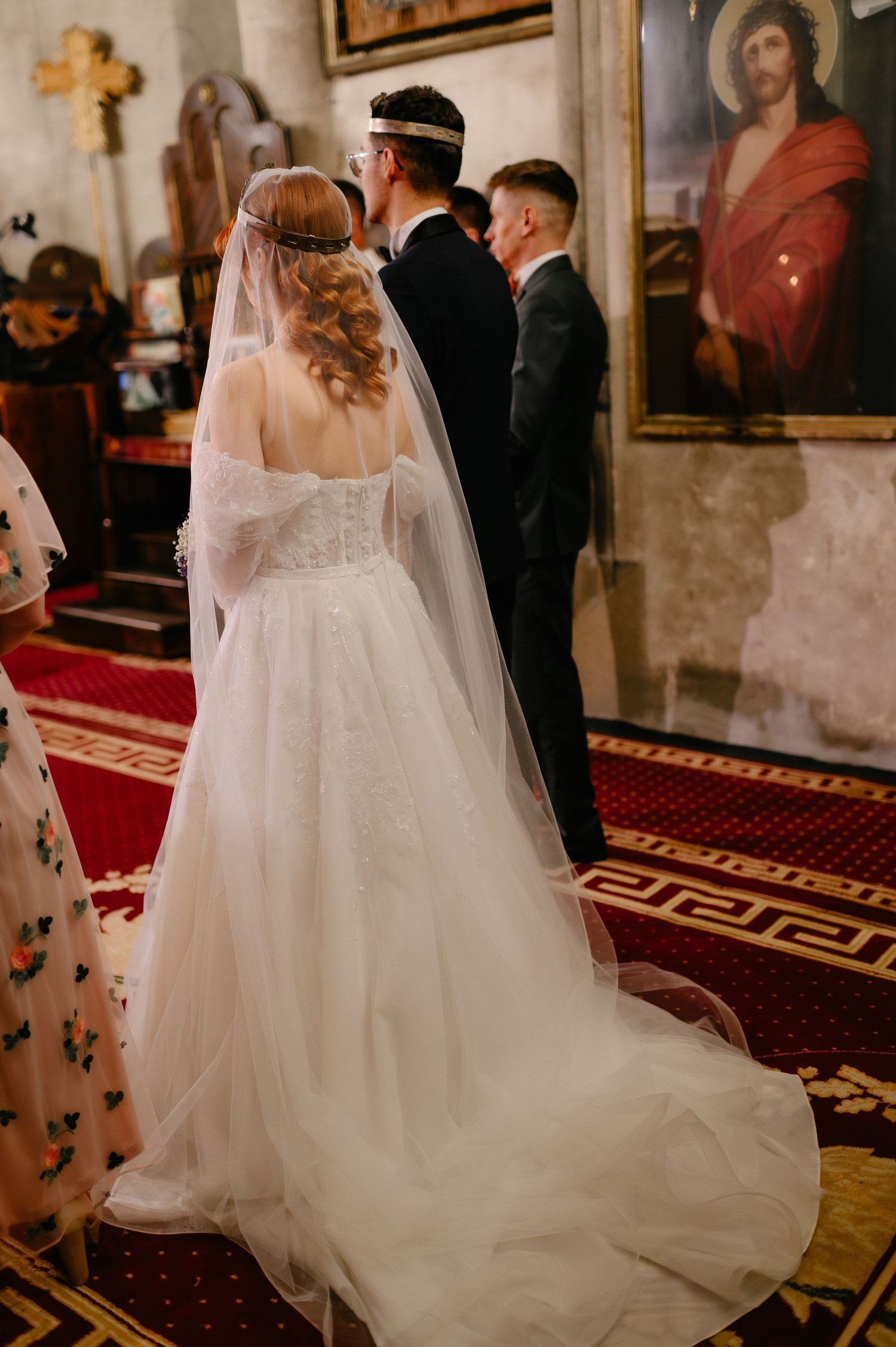 Bride in elegant white ball gown with veil stands at church altar during wedding ceremony with groom and officiant.
