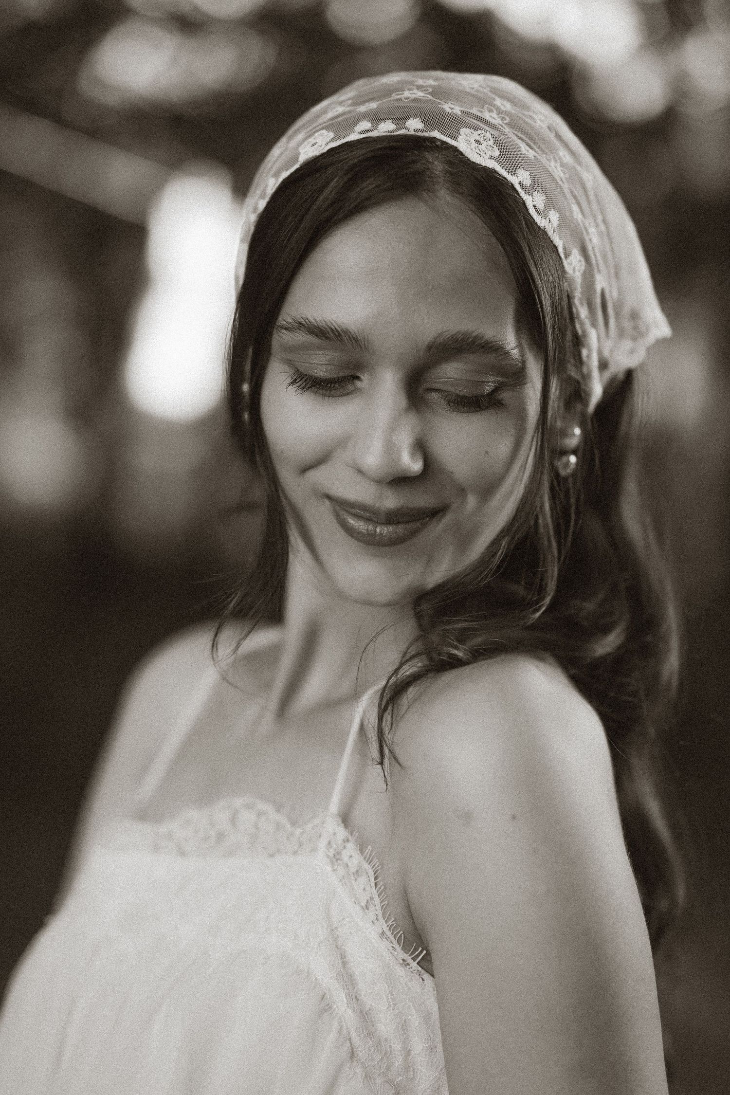 Black and white portrait of a smiling bride wearing a lace veil headpiece and white dress, eyes gently closed.