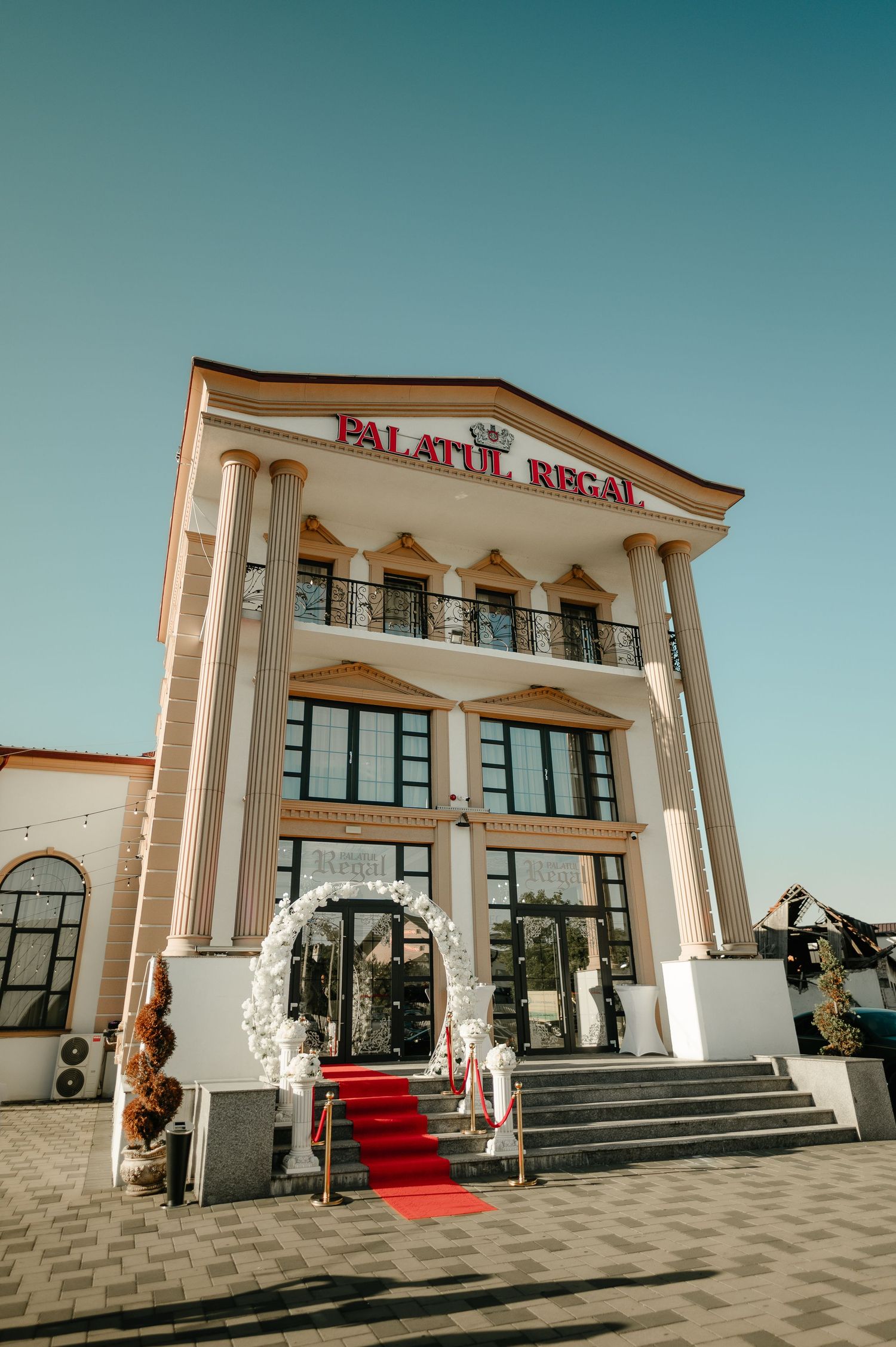 Palatul Regal wedding venue exterior with red carpet entrance, floral arch, and neoclassical facade.