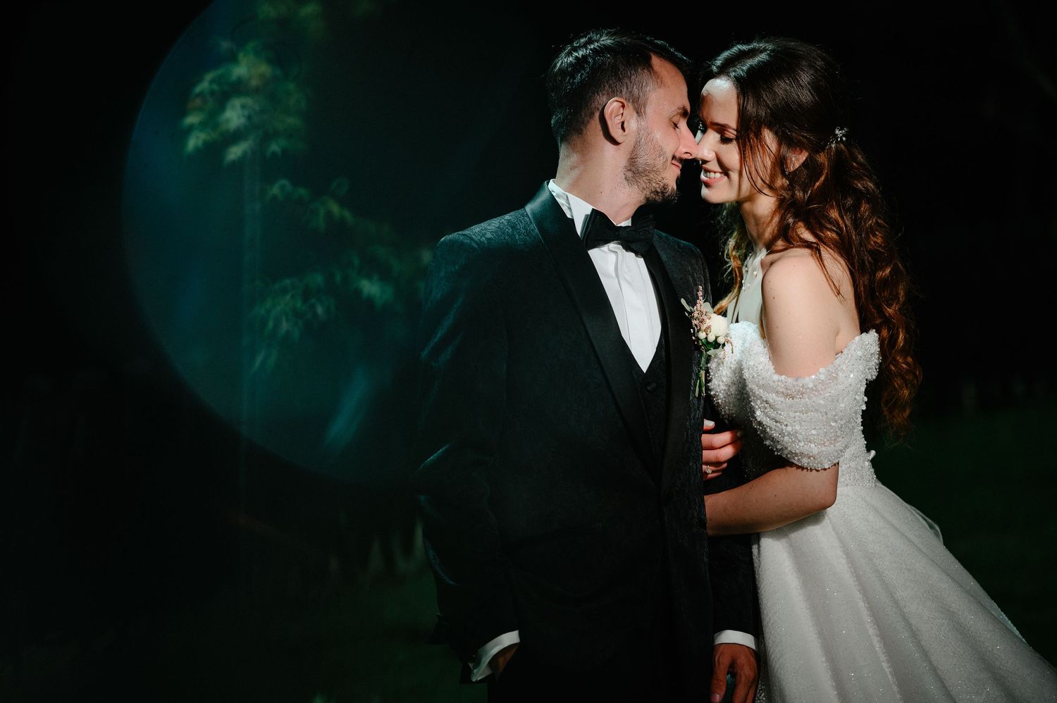 Bride and groom sharing romantic moment under spotlight in elegant dark wedding venue.