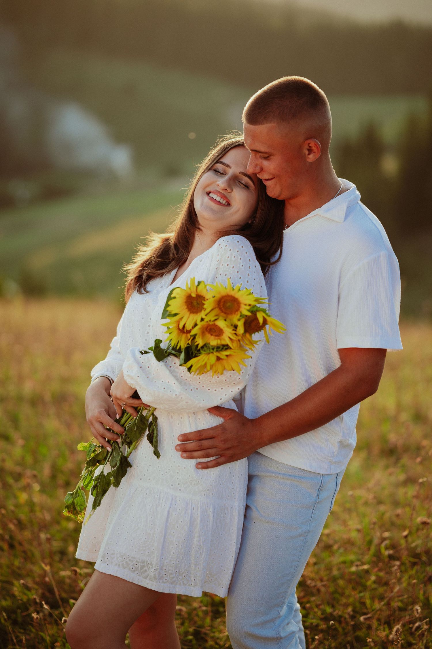 Joyful couple embracing with sunflowers laughing together in a warm sunset meadow.