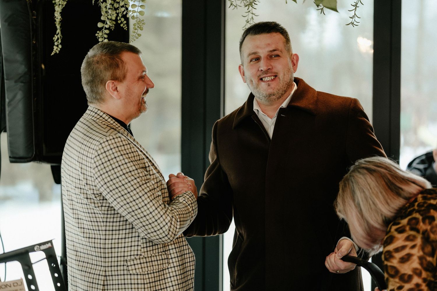 Two men in suits shaking hands and smiling at a formal indoor celebration event.