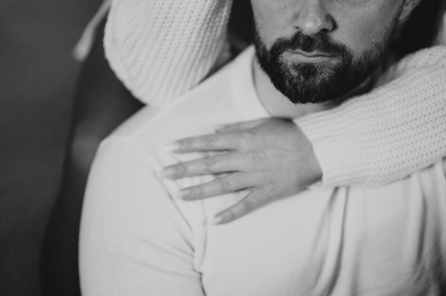 Black and white close-up of a couple embracing, woman's hand resting on man's shoulder.