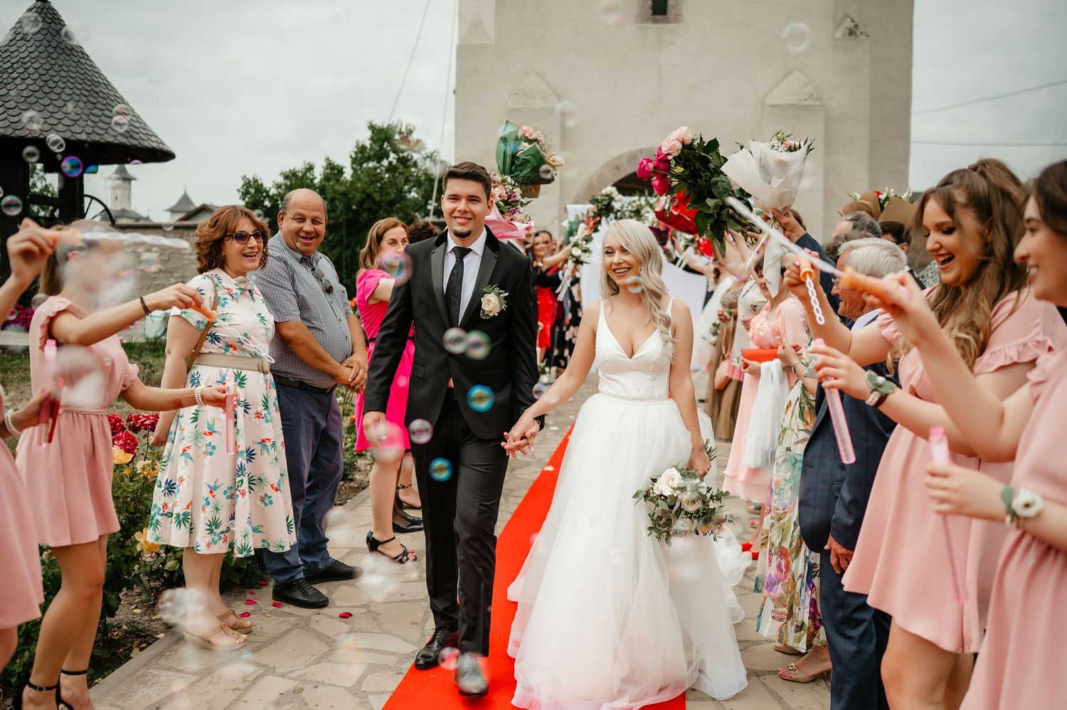 Newlyweds walk down the aisle as guests blow bubbles in celebration outside a white church.