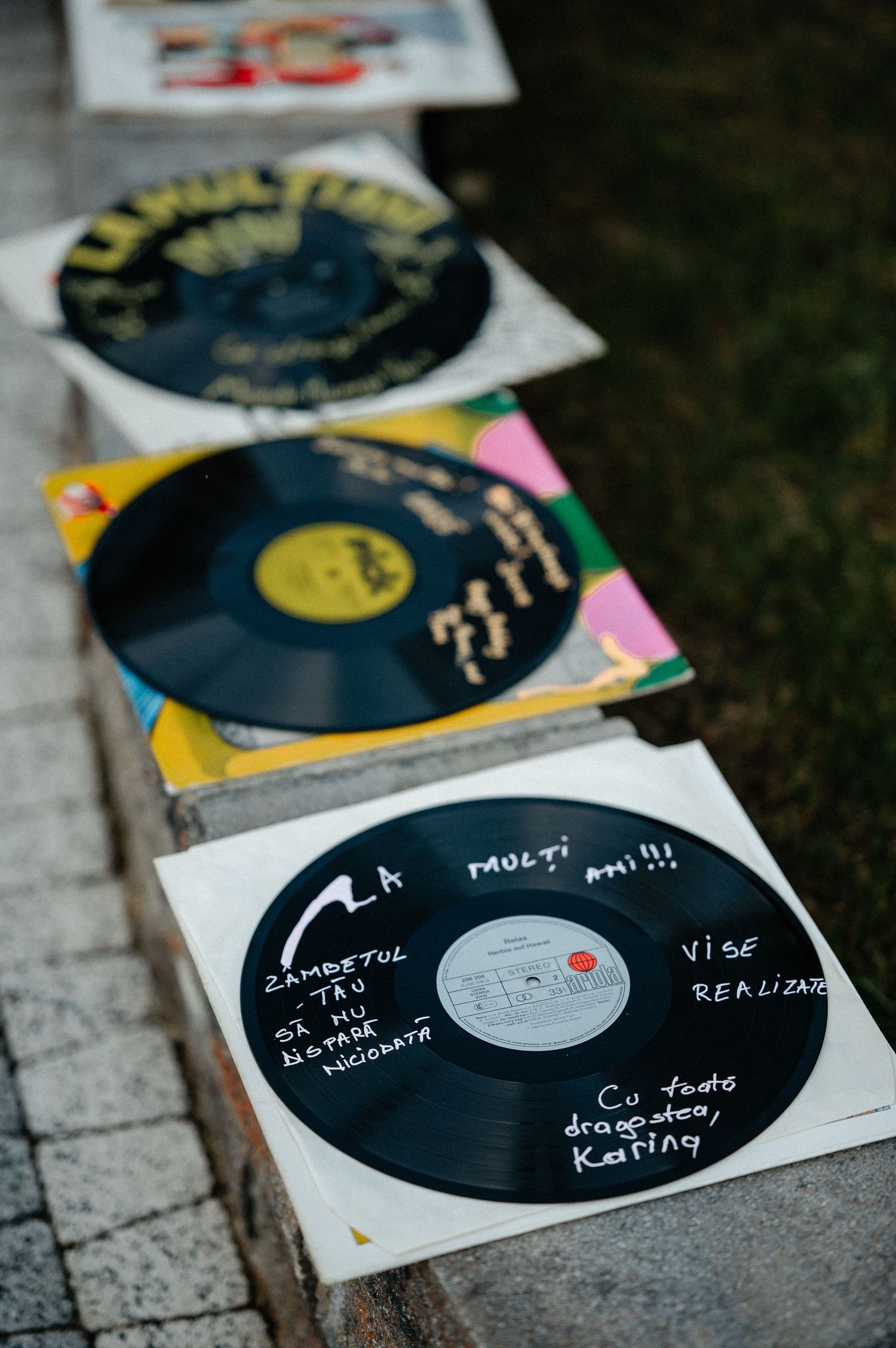 Close-up of vinyl records with handwritten birthday wishes displayed outdoors on a stone ledge.