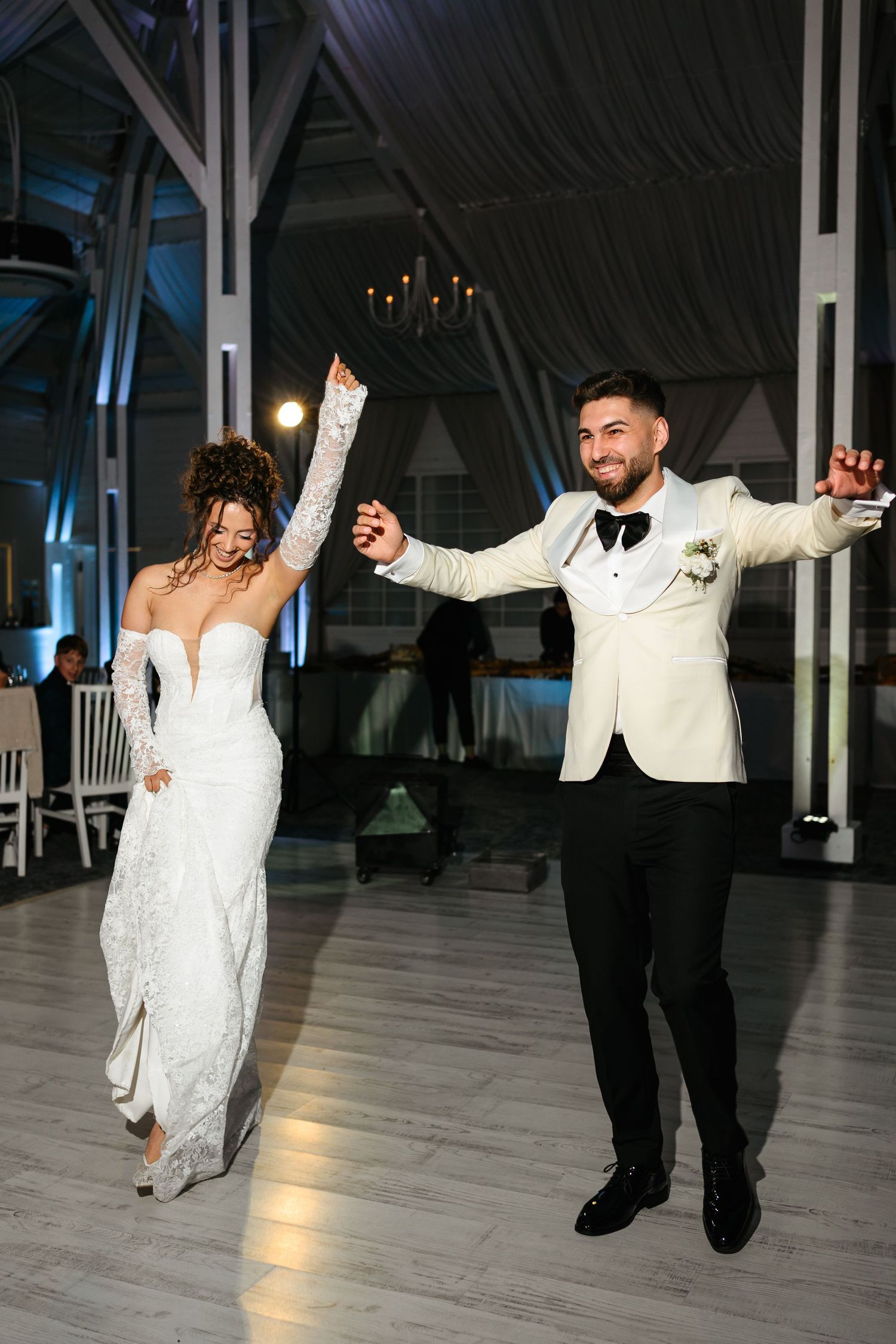 Bride and groom share joyful first dance in elegant wedding venue with blue lighting and draped ceilings.