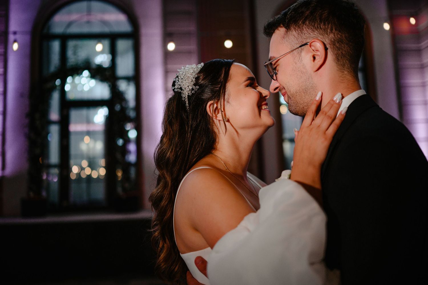 Bride and groom share a romantic close moment under purple ambient lighting at wedding reception.