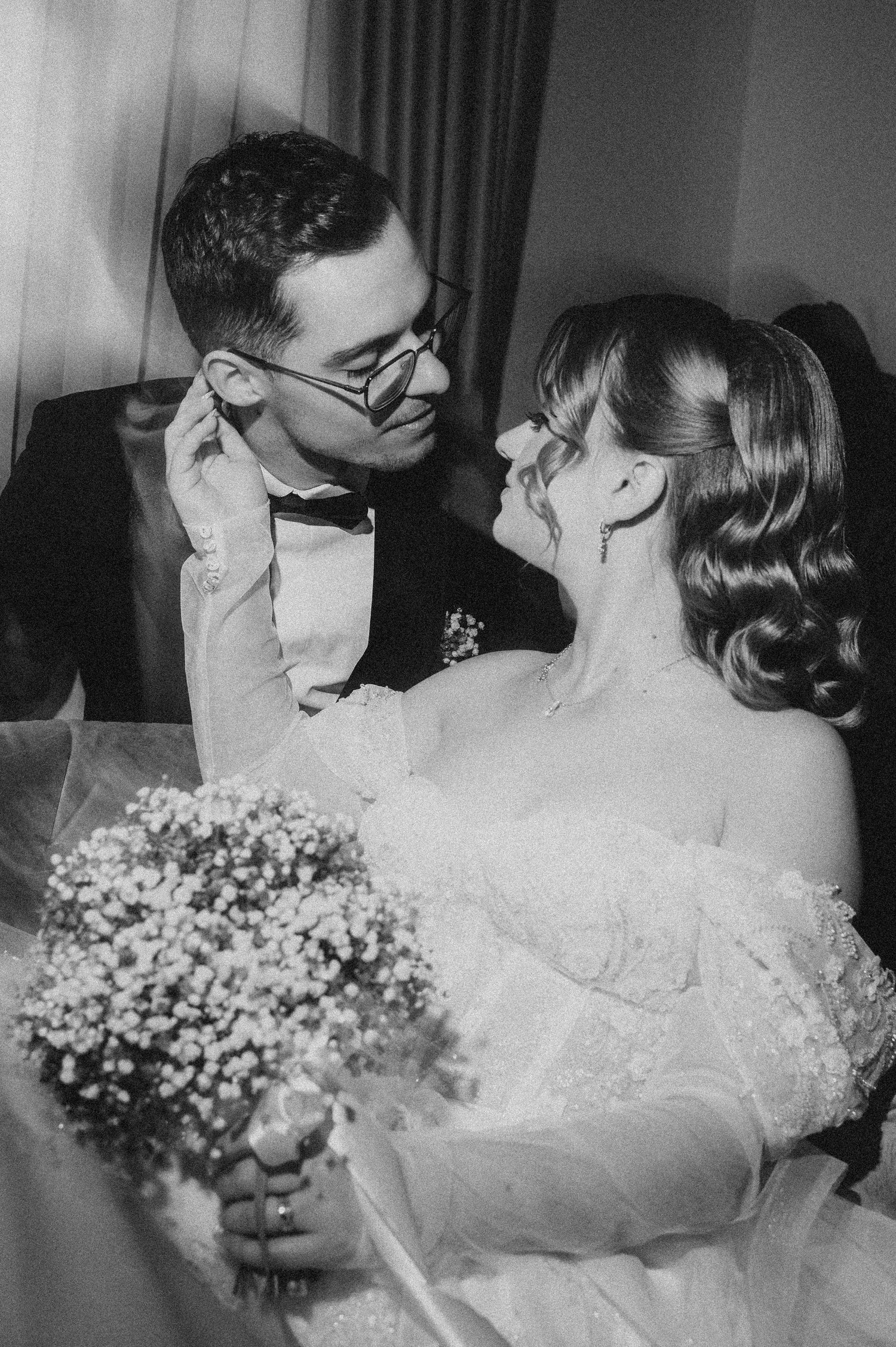 Black and white wedding photo of bride holding bouquet and groom in bow tie sharing a romantic moment.