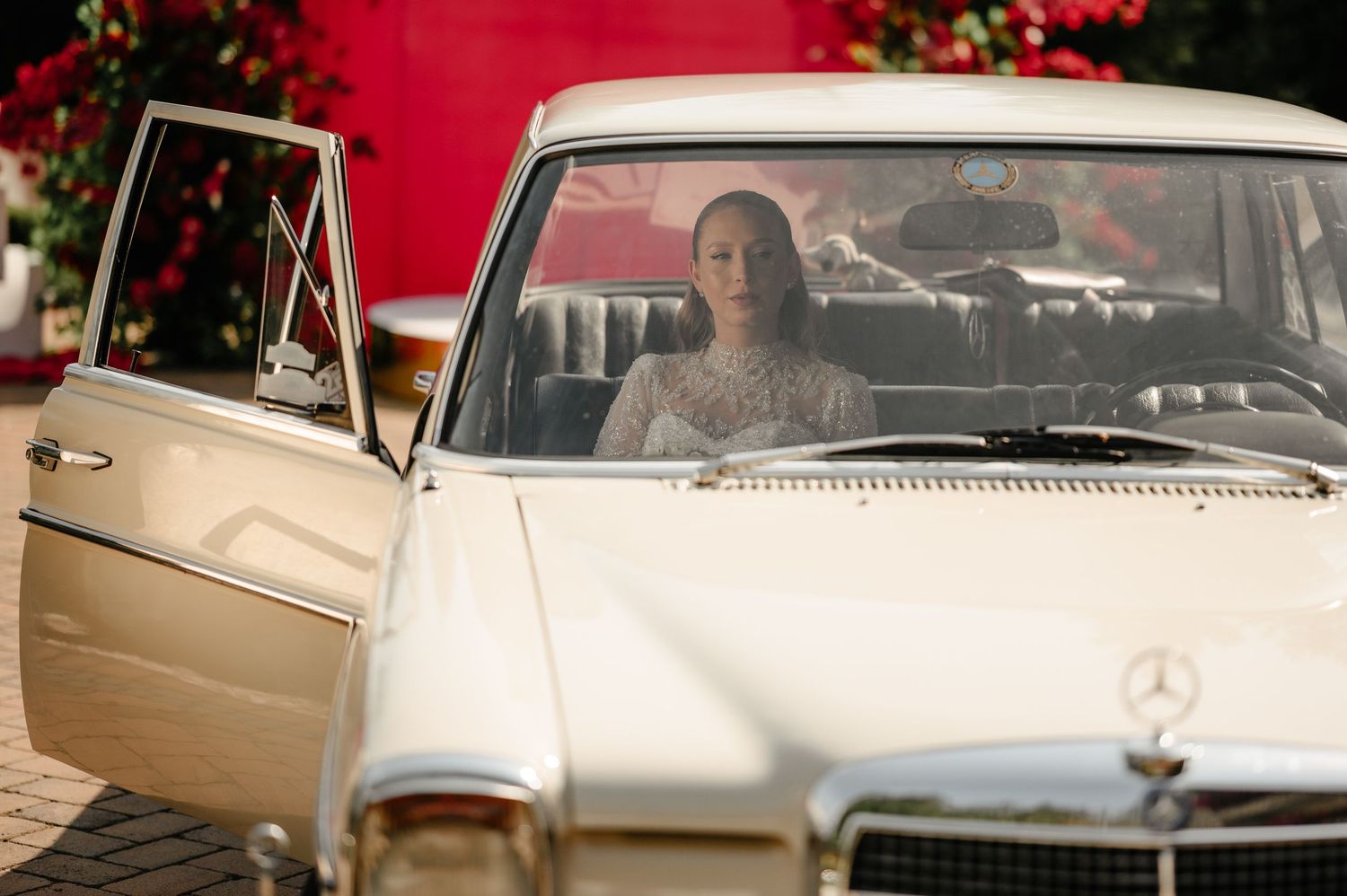 Bride in lace wedding dress sitting inside a classic white vintage Mercedes-Benz wedding car.
