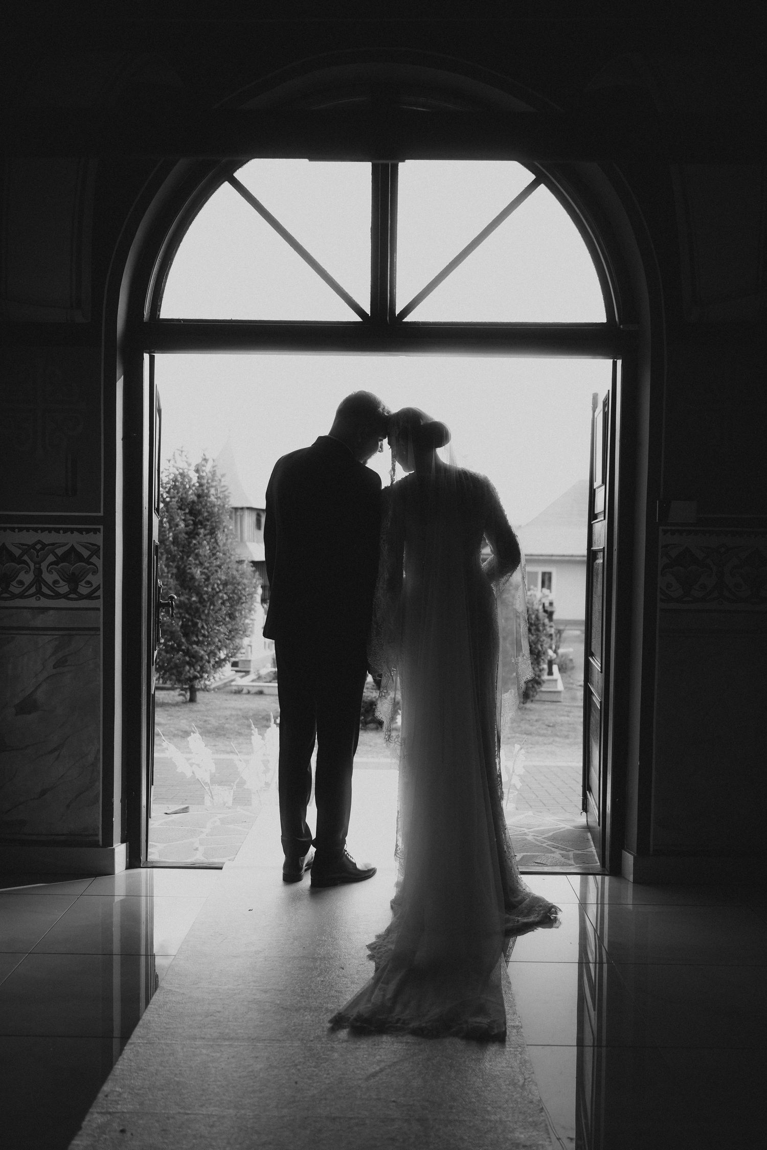 Black and white silhouette of bride and groom sharing intimate moment in arched doorway at elegant wedding venue.
