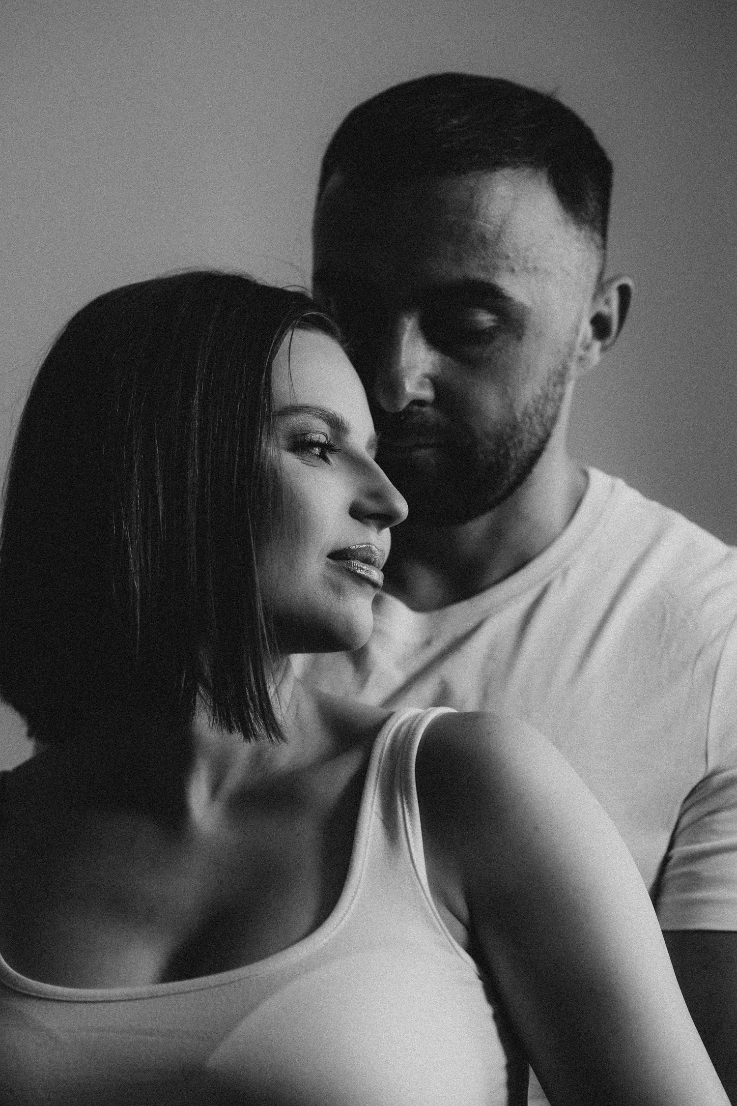 Intimate black and white portrait of a couple, woman in tank top with bearded man standing close behind her.