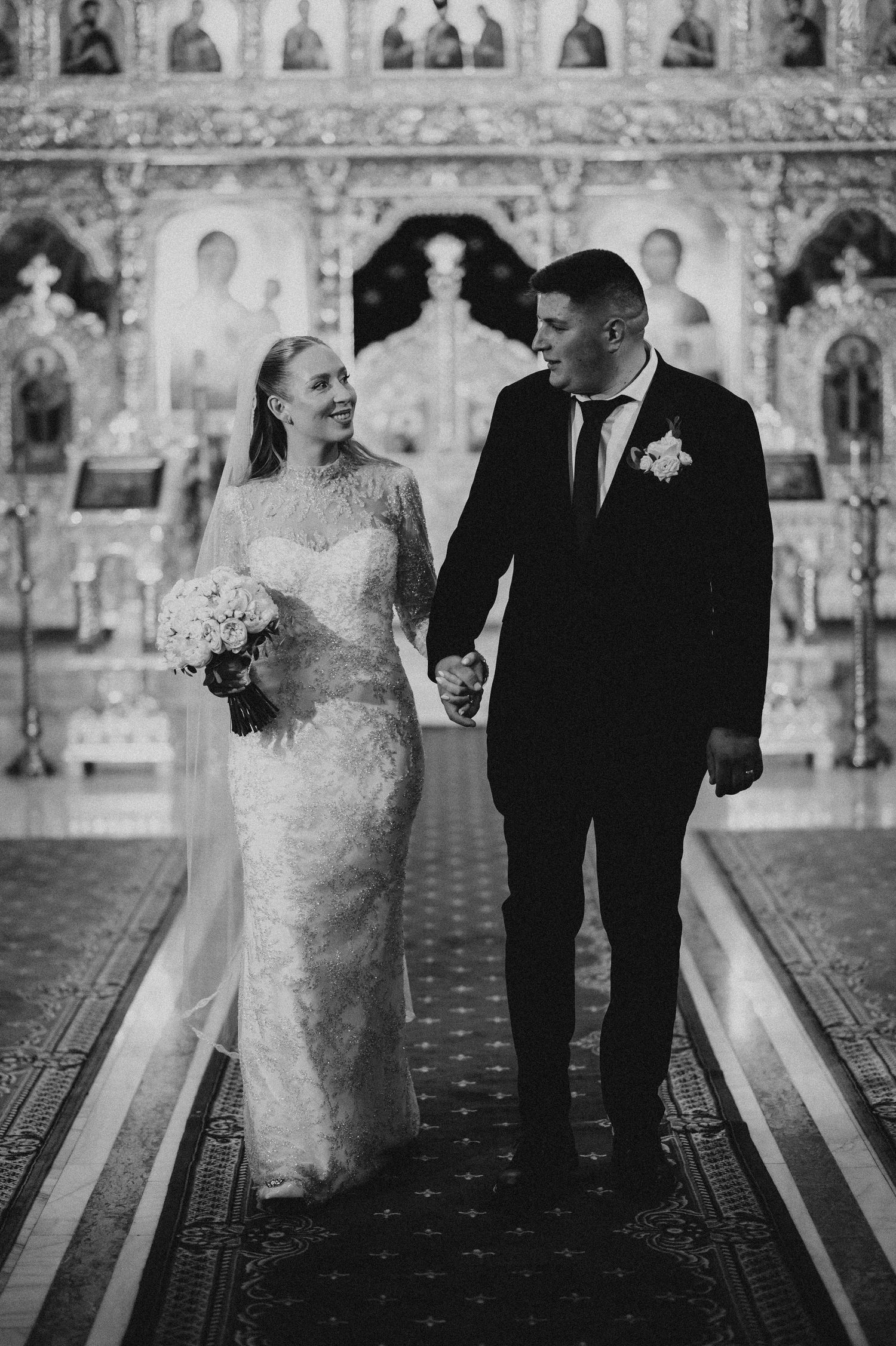 Bride and groom holding hands walking down church aisle in black and white.