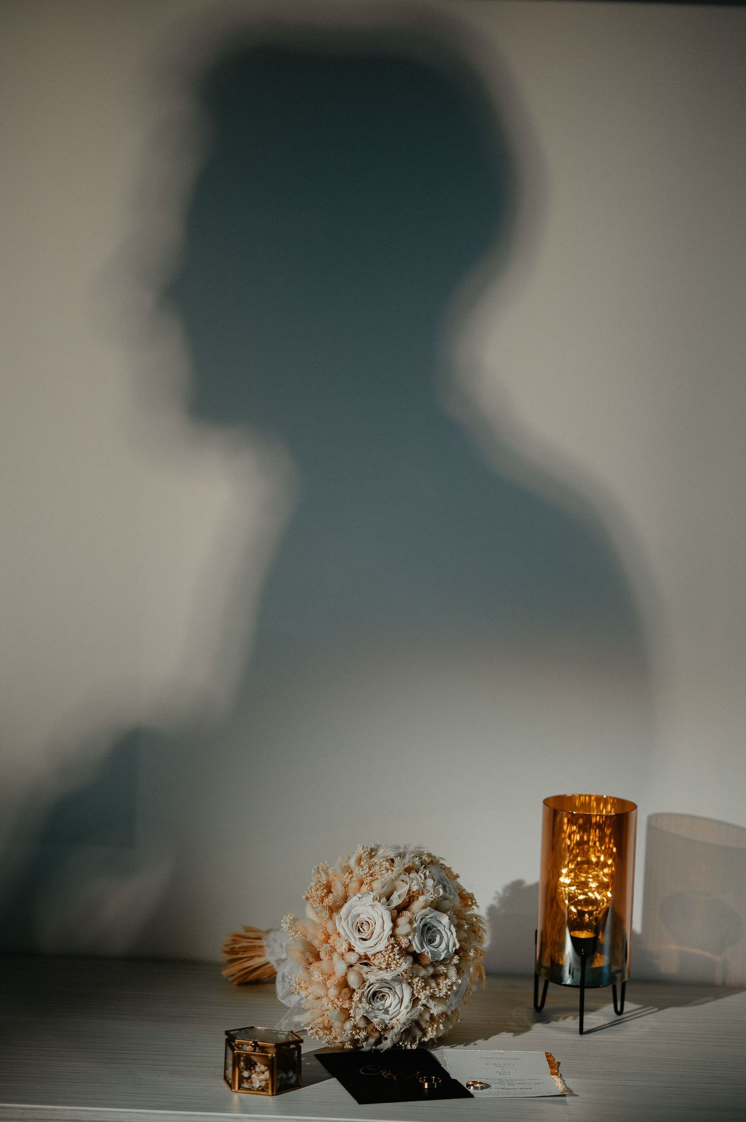Wedding bouquet and amber candle holder on a table with a silhouette shadow on the wall.