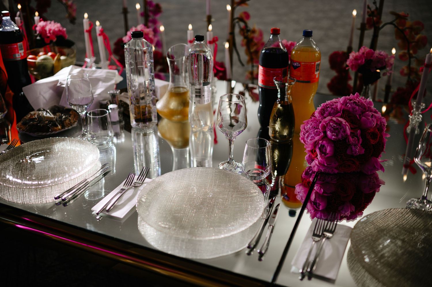 Elegant wedding table with mirrored surface, crystal plates, pink roses, candles, and glassware.