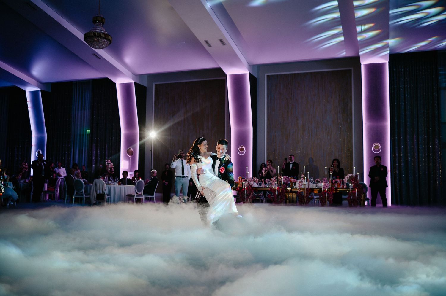 Bride and groom share romantic first dance on fog-filled dance floor with purple uplighting at wedding.
