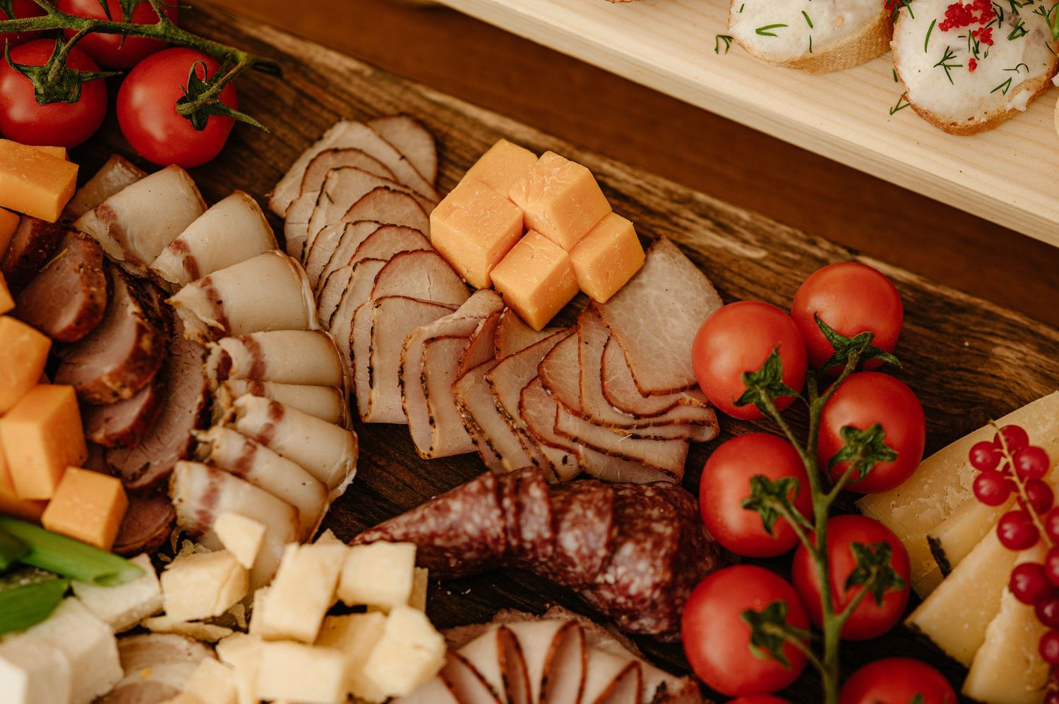 Elegant charcuterie board with sliced meats, cheese cubes, and fresh cherry tomatoes.