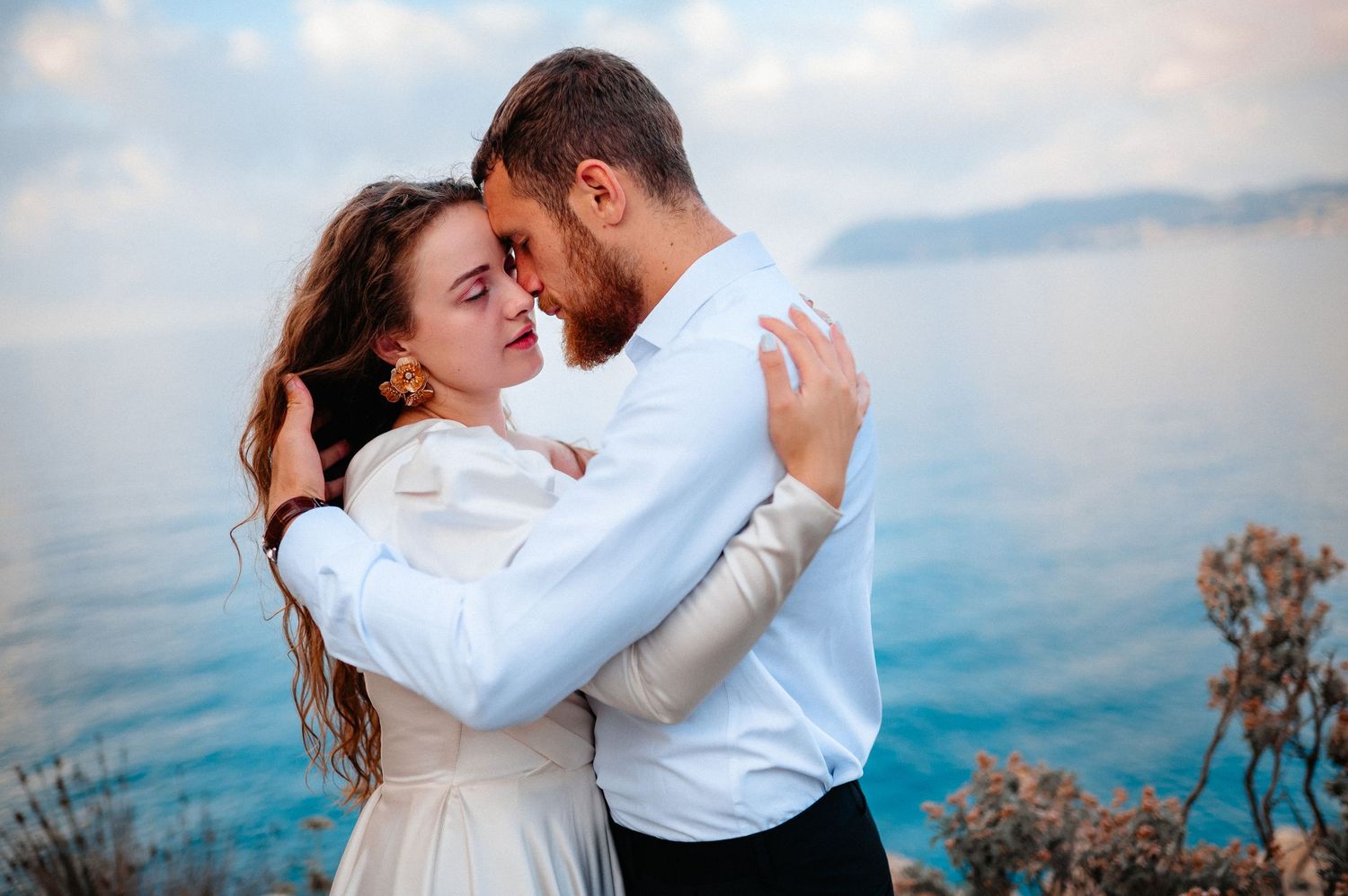 Romantic couple embracing with forehead touch against stunning blue sea backdrop.