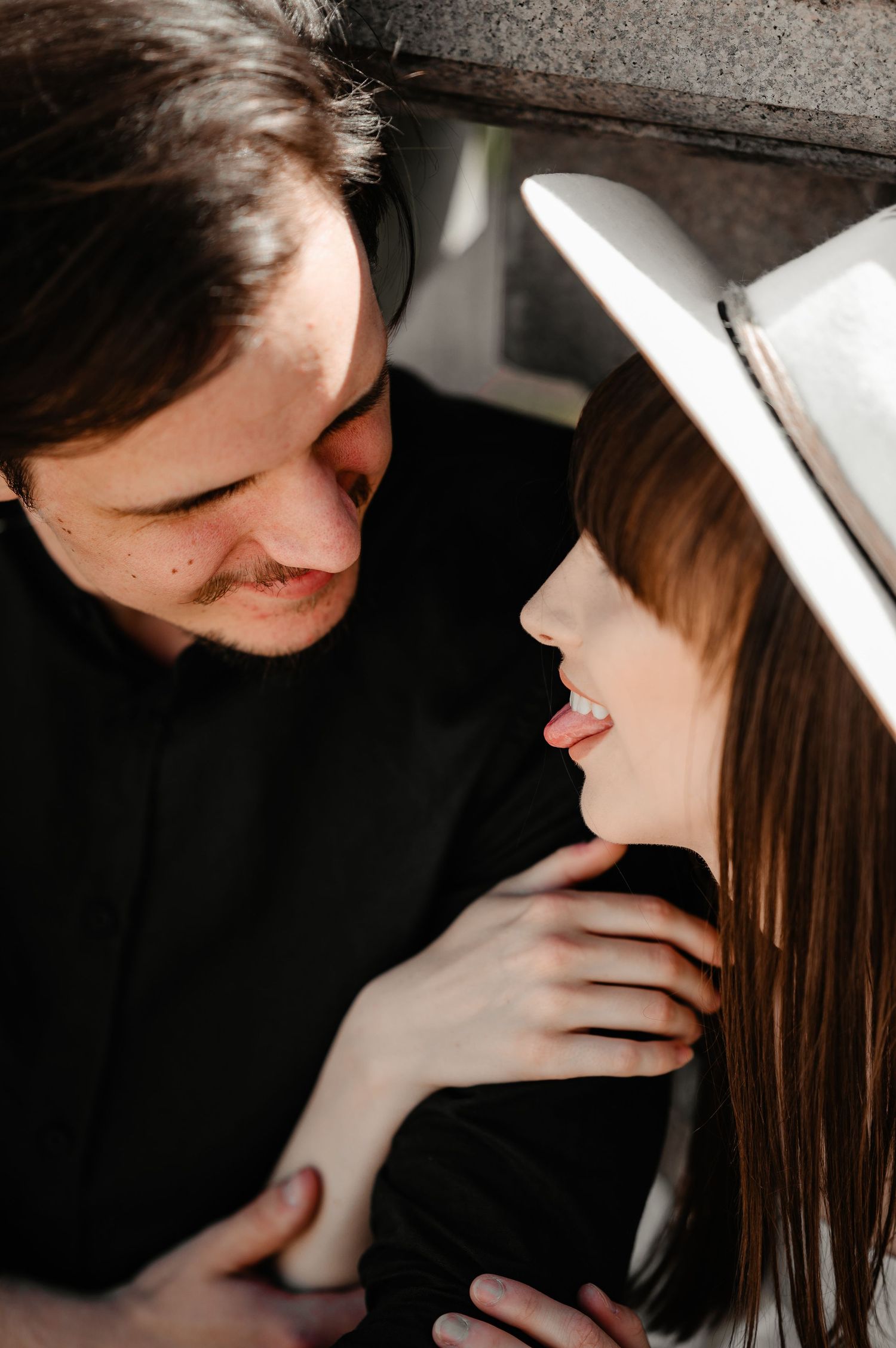 Romantic close-up of a smiling couple gazing at each other, woman wearing a white wide-brim hat.