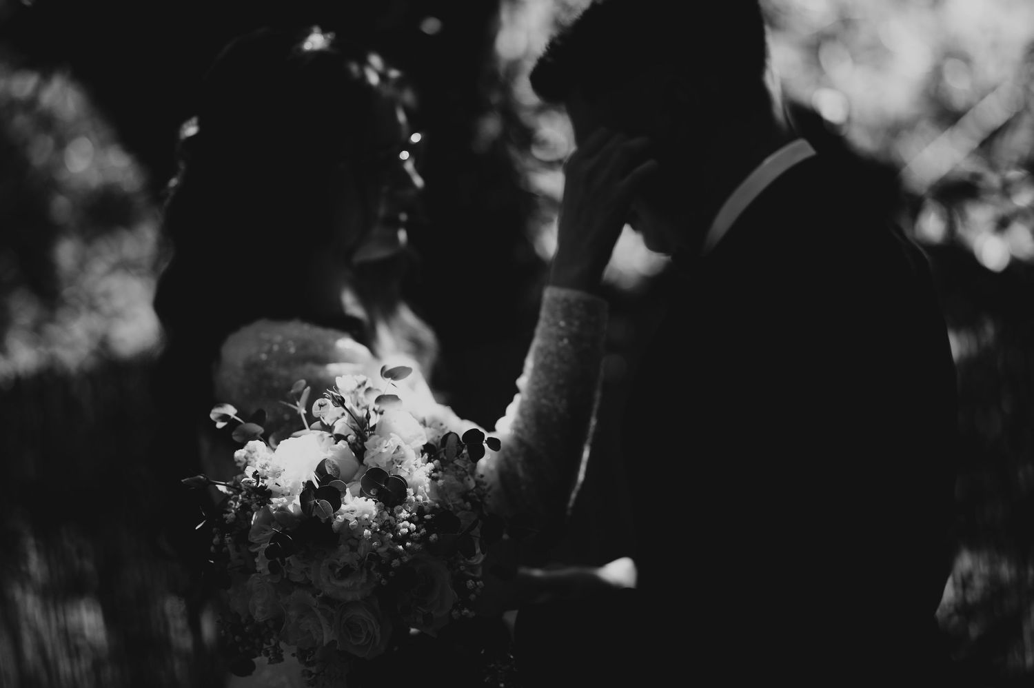 Black and white photo of bride and groom sharing an emotional moment with wedding bouquet.