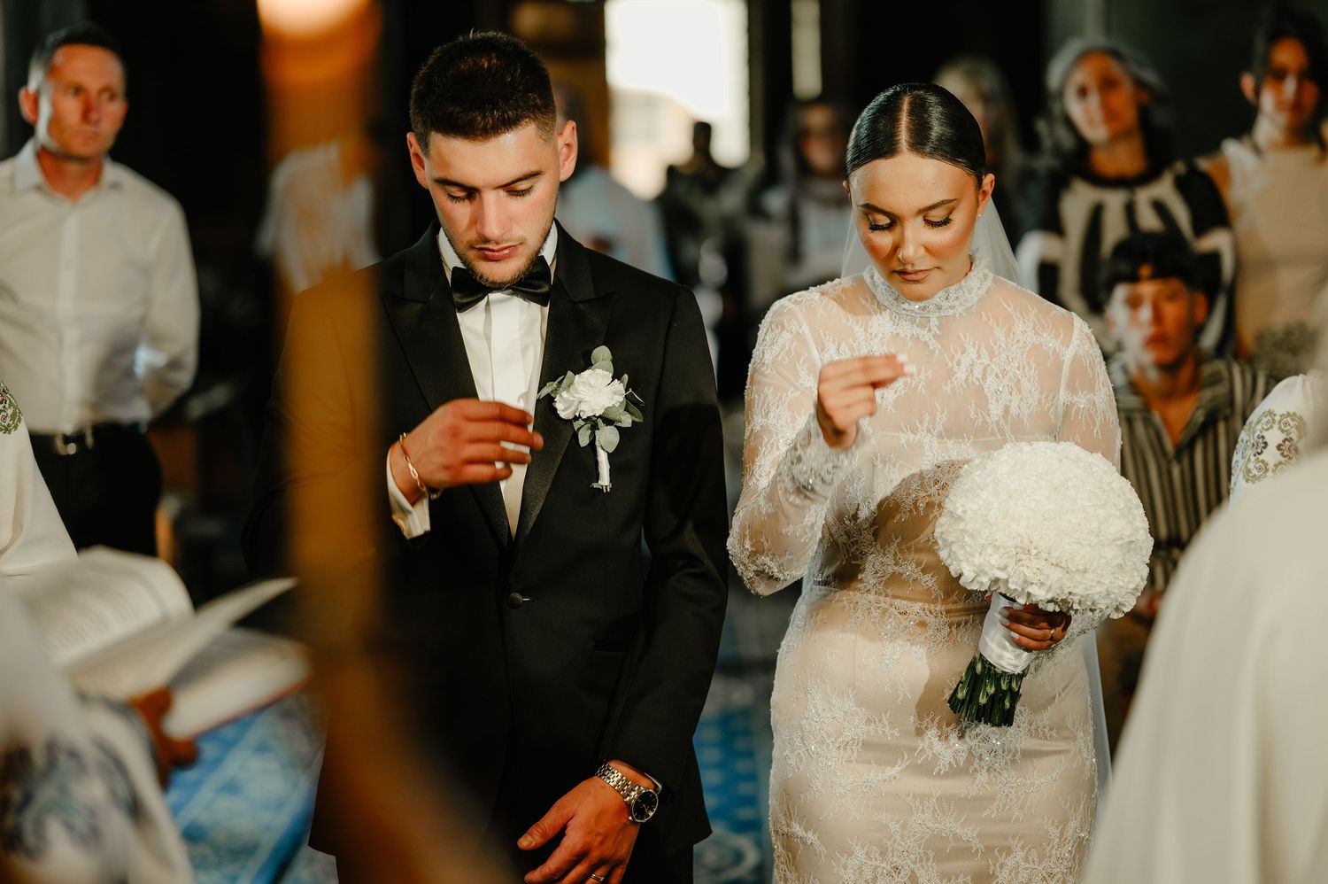 Bride and groom standing solemnly during Orthodox church wedding ceremony with candles.