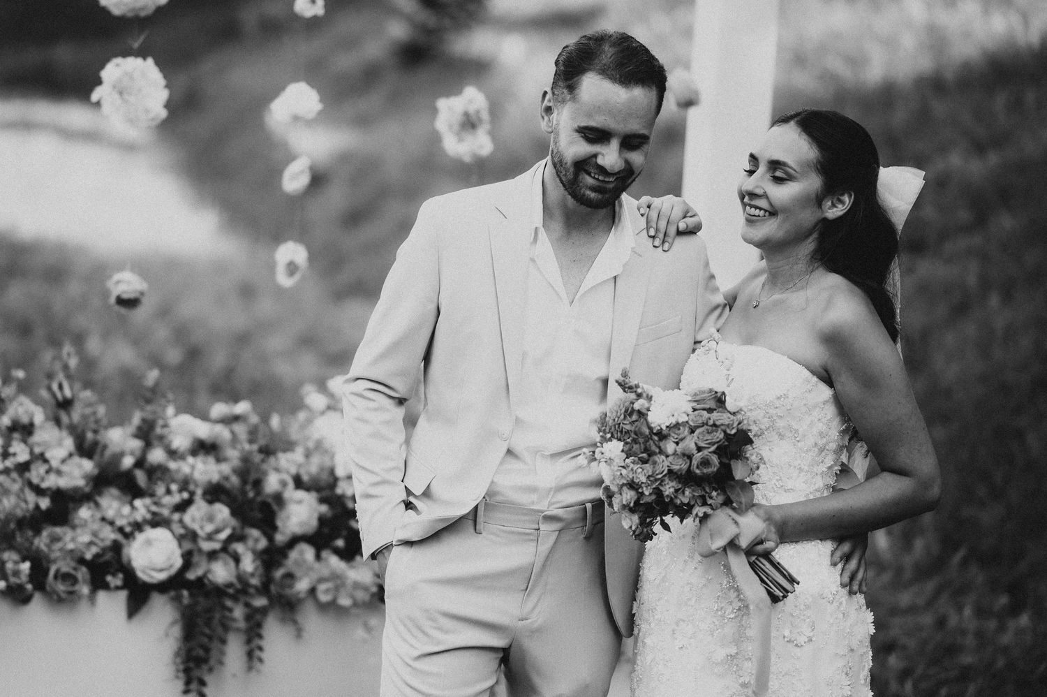 Black and white photo of laughing newlyweds posing together at their outdoor wedding ceremony.