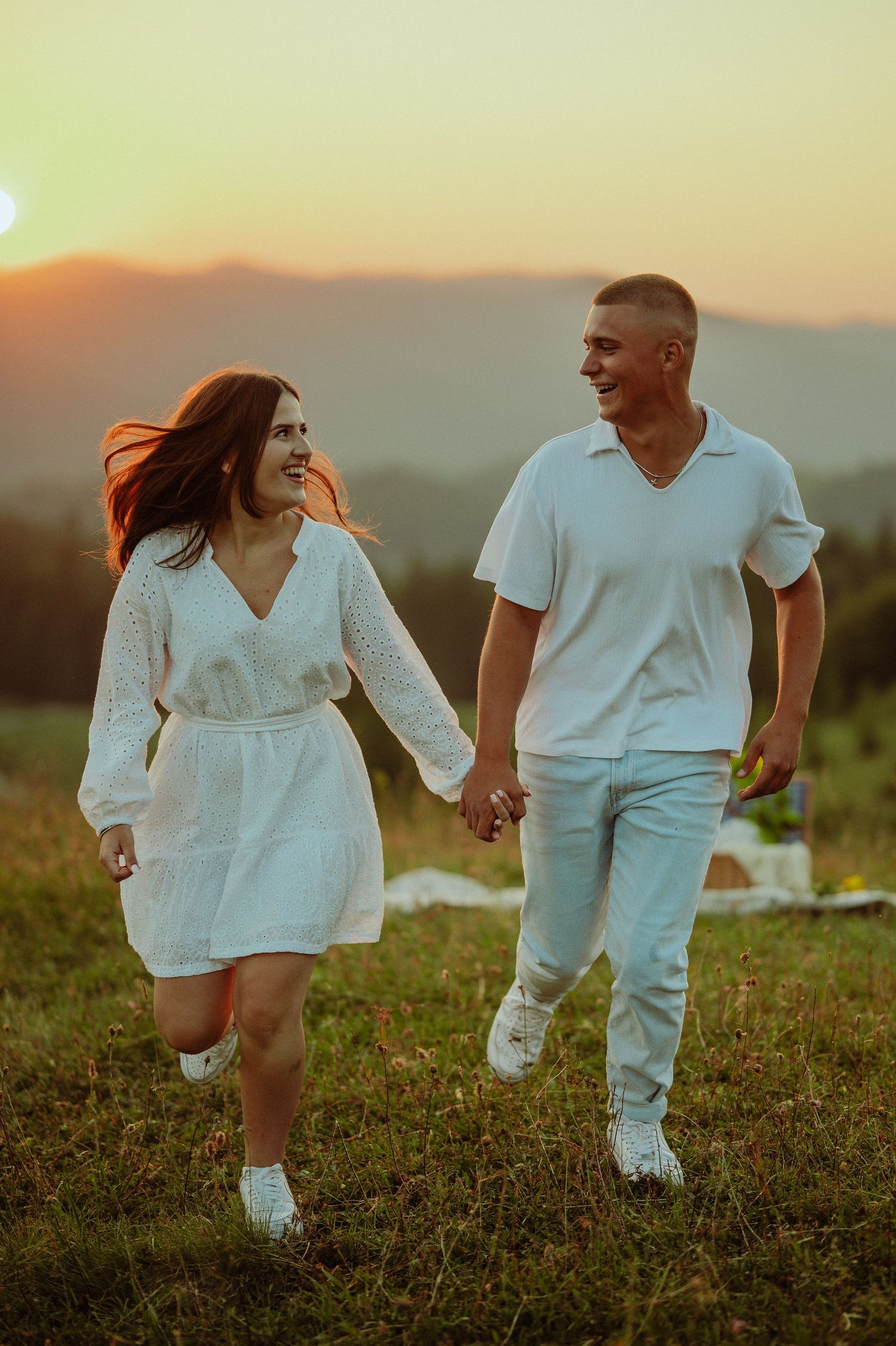 Joyful couple running hand-in-hand through a meadow at golden sunset in the mountains.