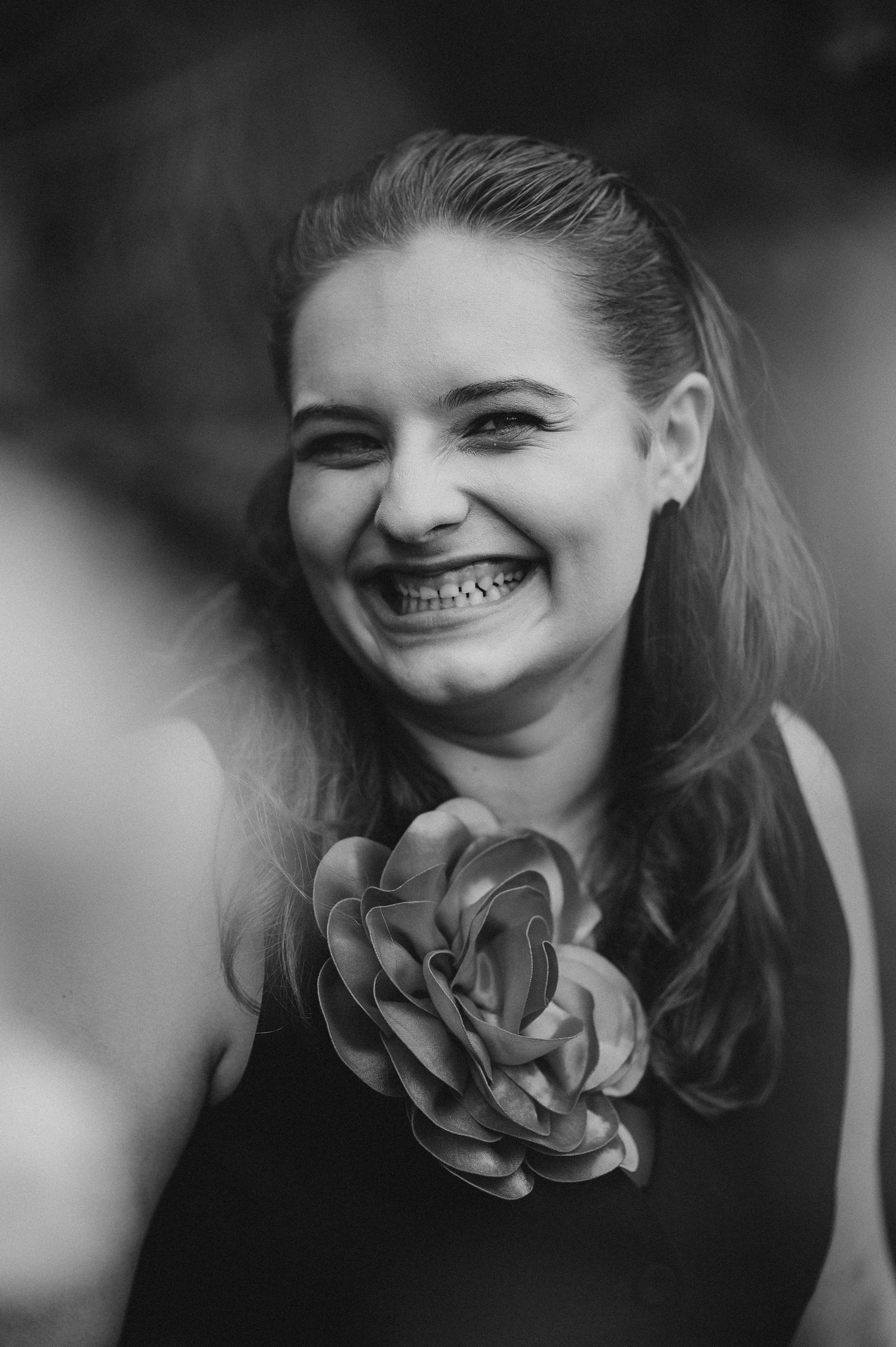 Smiling young woman with braces holding a large flower corsage in a black and white portrait photo.