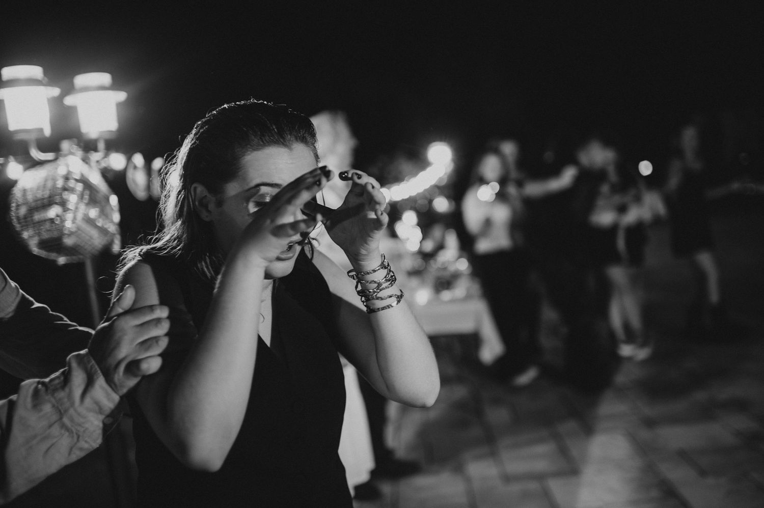 Black and white photo of a young woman wiping tears at an emotional outdoor night celebration.