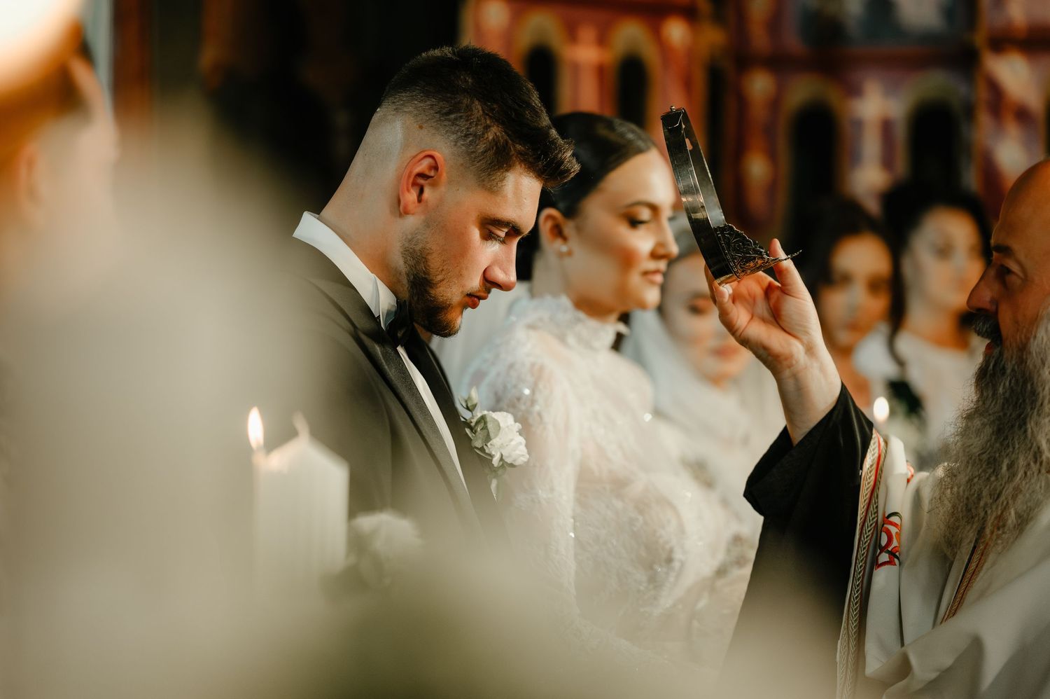 Bride and groom bow heads during Orthodox Christian wedding ceremony with priest holding a cross.