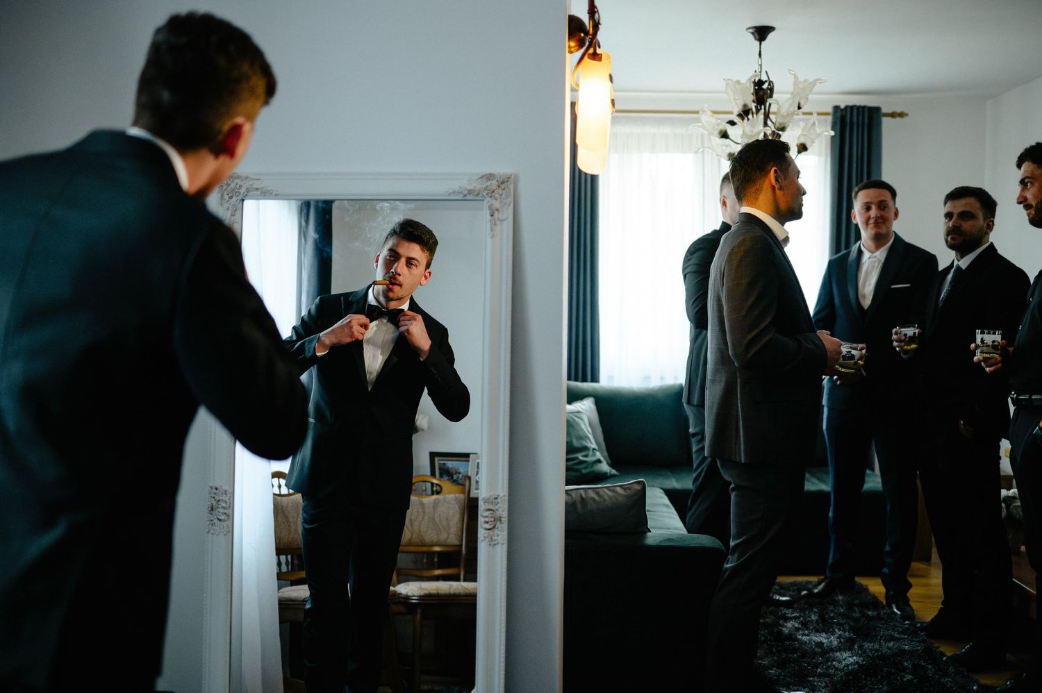 Groom adjusting his tie in a mirror while groomsmen prepare in the background.