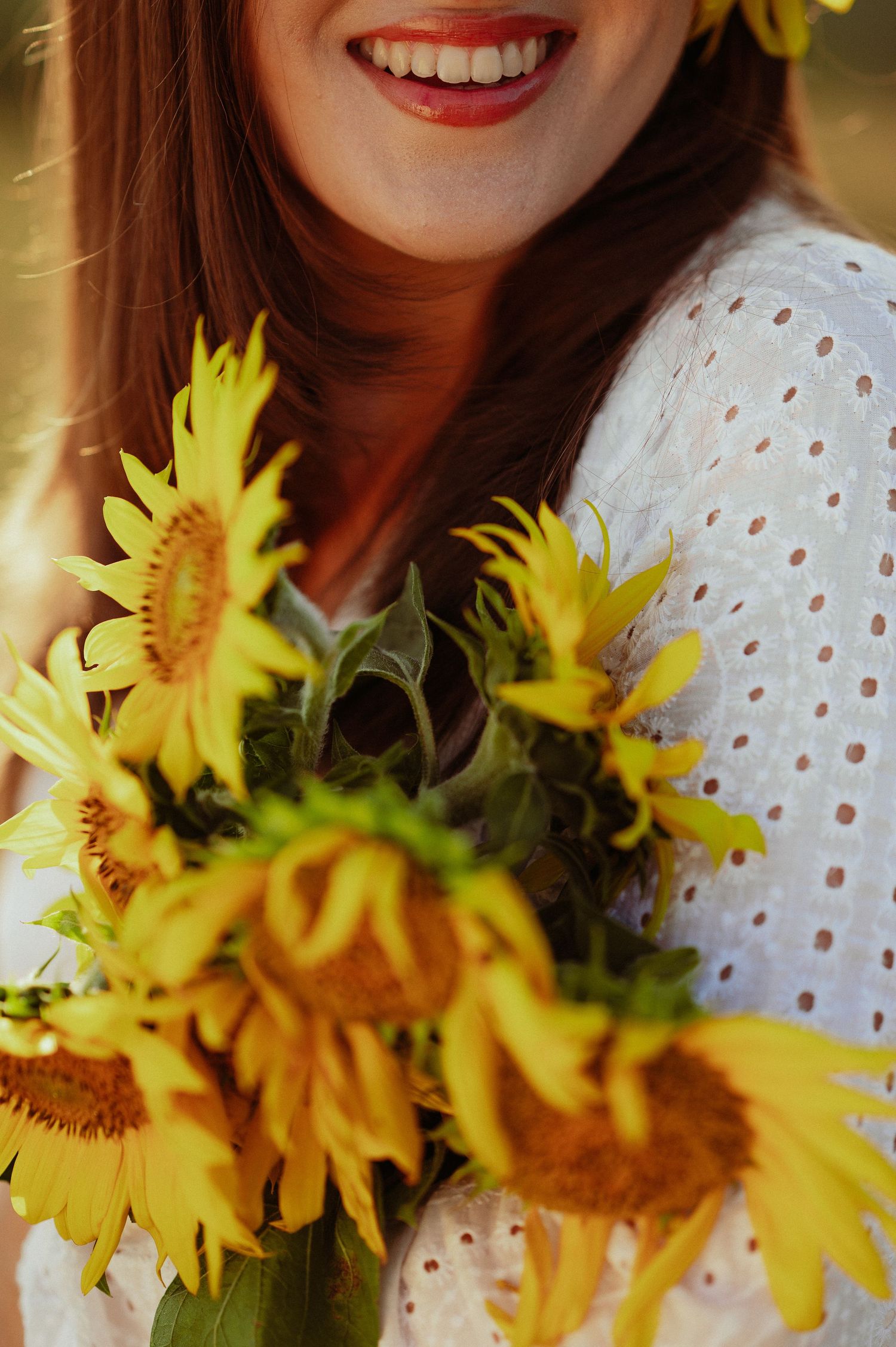 Close-up of smiling woman in white dress holding vibrant yellow sunflower bouquet.