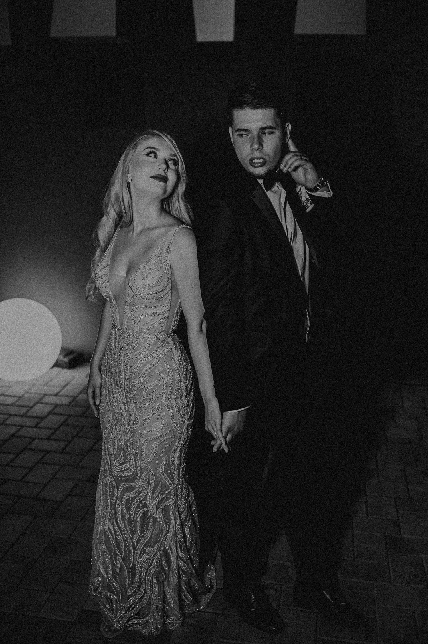 Black and white portrait of a bride in a beaded gown and groom in a tuxedo posing outdoors.