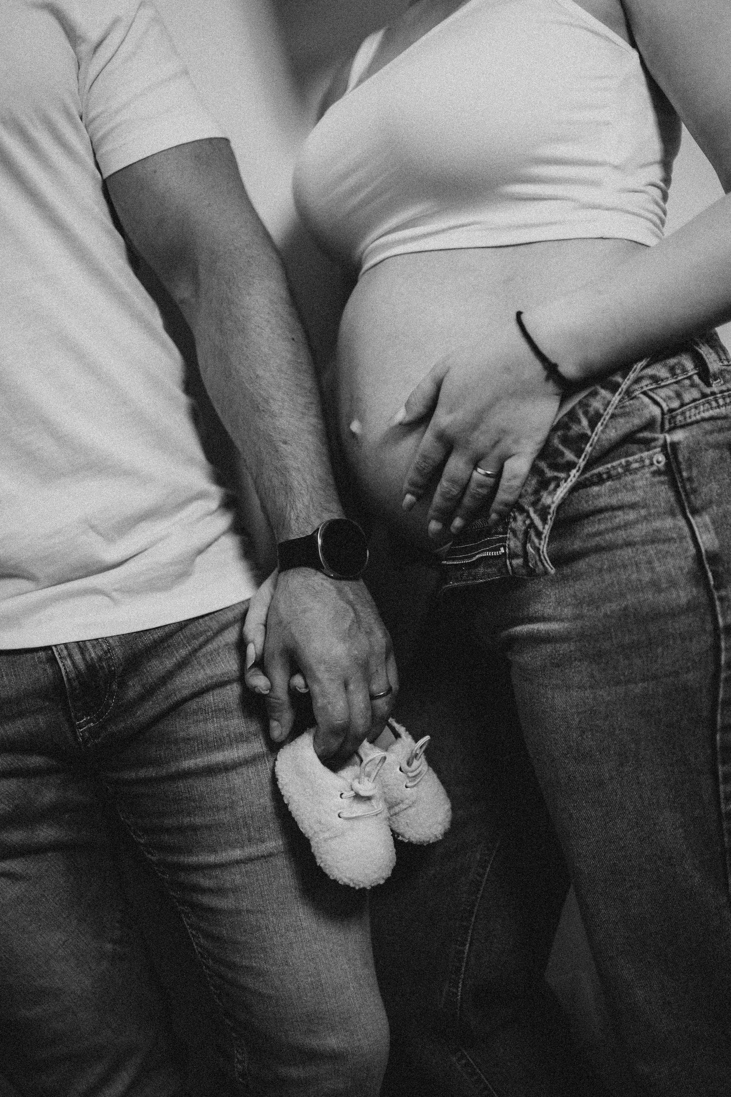 Couple holding tiny baby shoes next to pregnant belly in black and white close-up maternity photo.