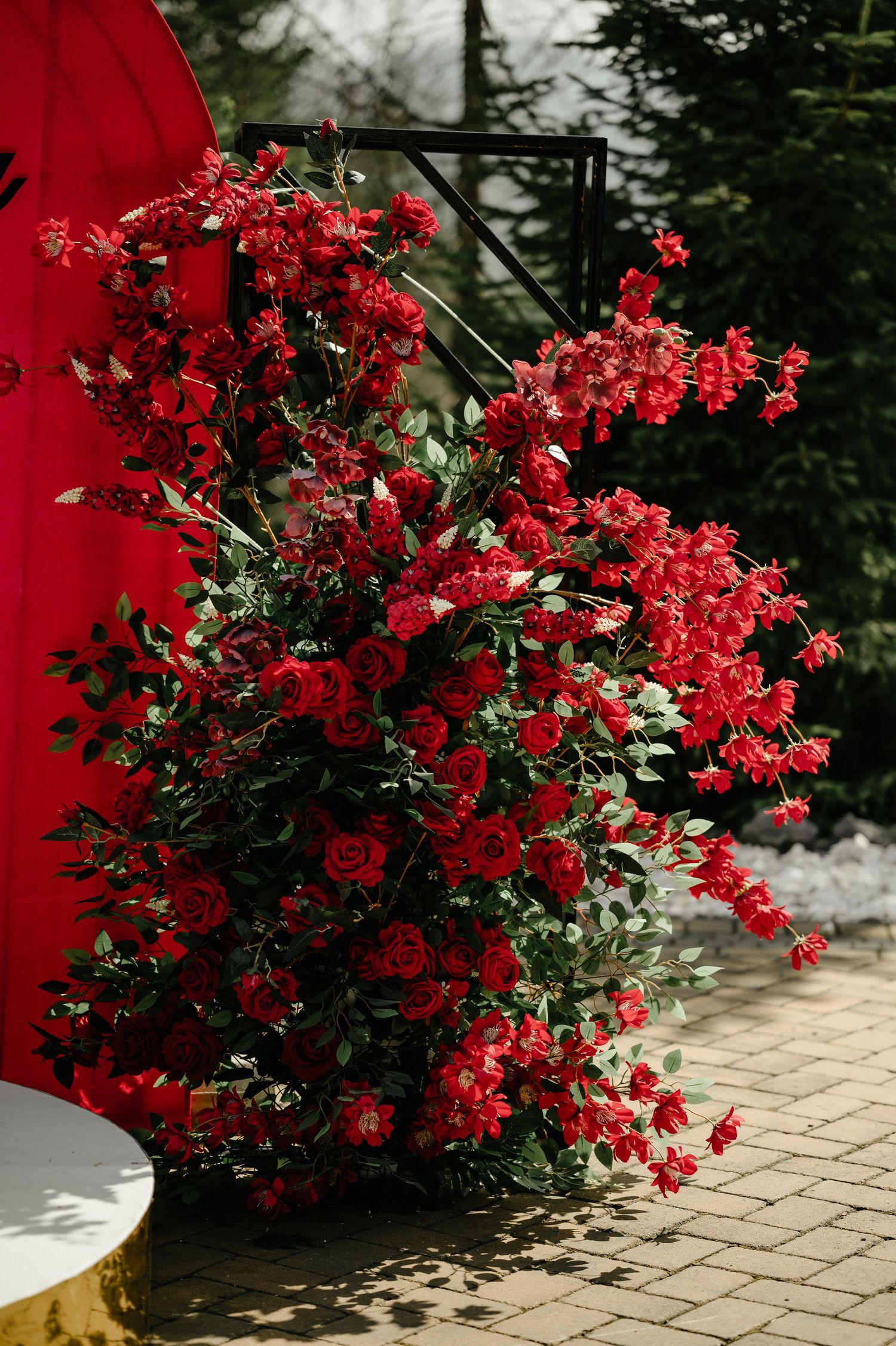 Stunning large floral arrangement of red roses and greenery at outdoor wedding ceremony decor.