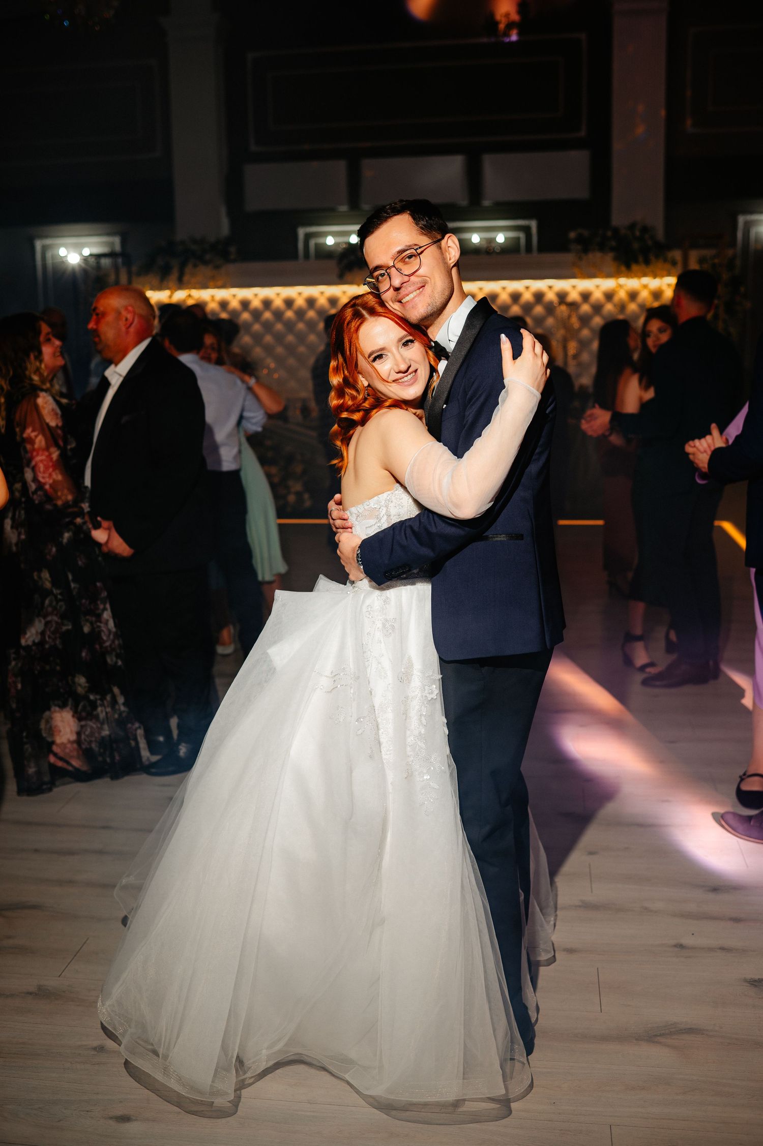 A bride in a white ball gown and groom in navy suit share their first dance at a wedding reception.