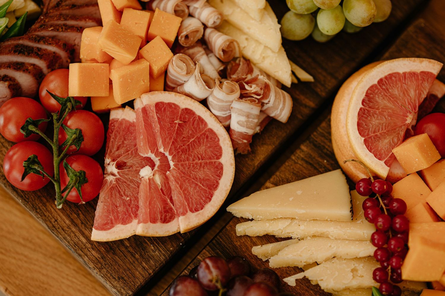 Rustic charcuterie board with grapefruit halves, assorted cheeses, meats, and fresh fruit.