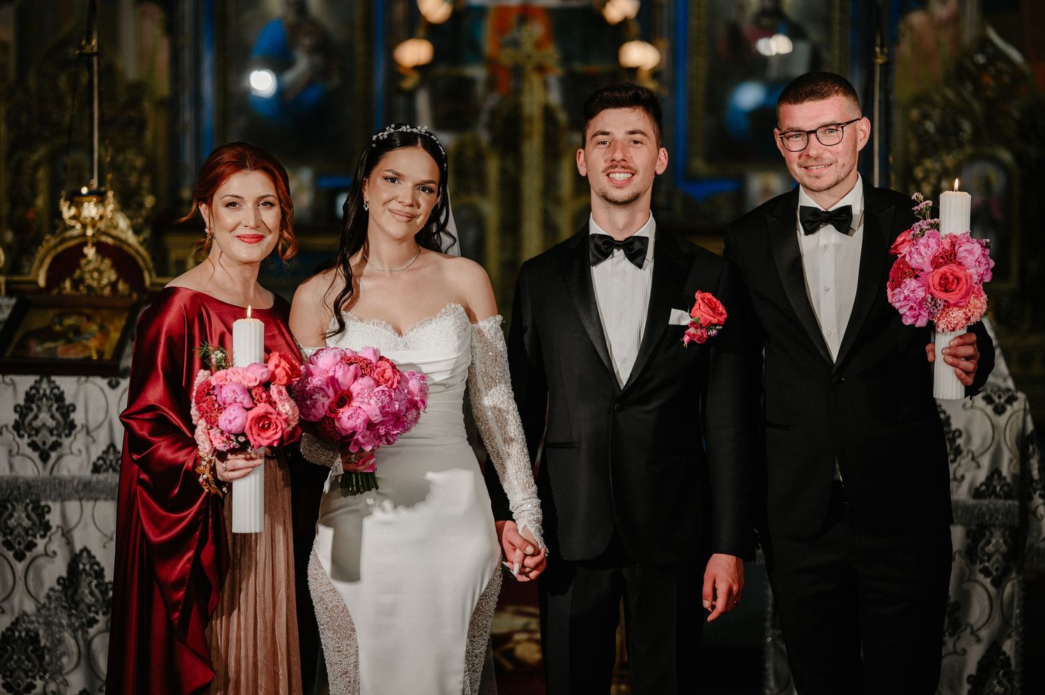 Wedding couple stands with godparents holding decorated candles during Orthodox church ceremony.