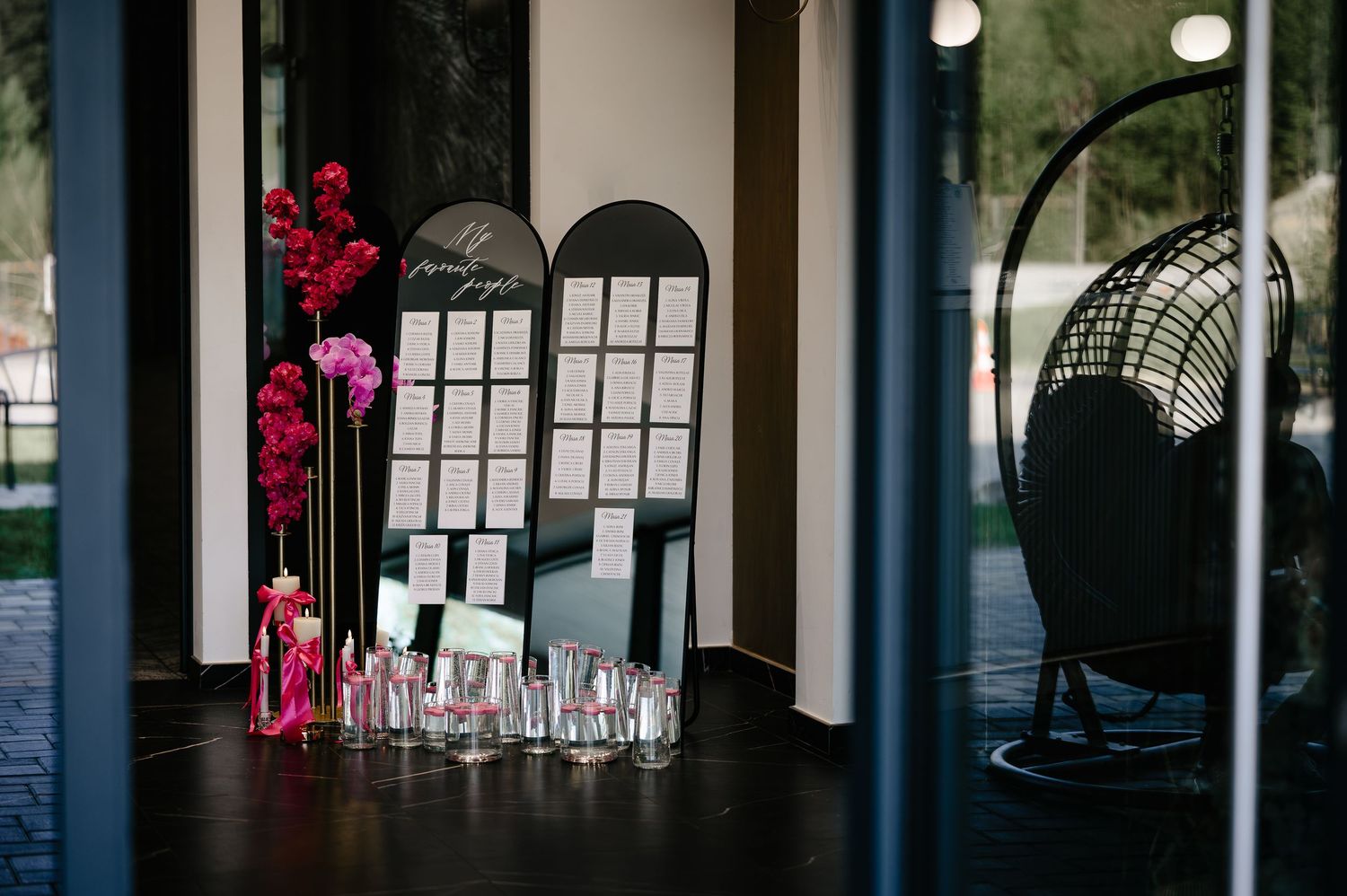Wedding seating chart display with arched black mirrors and pink floral arrangements.