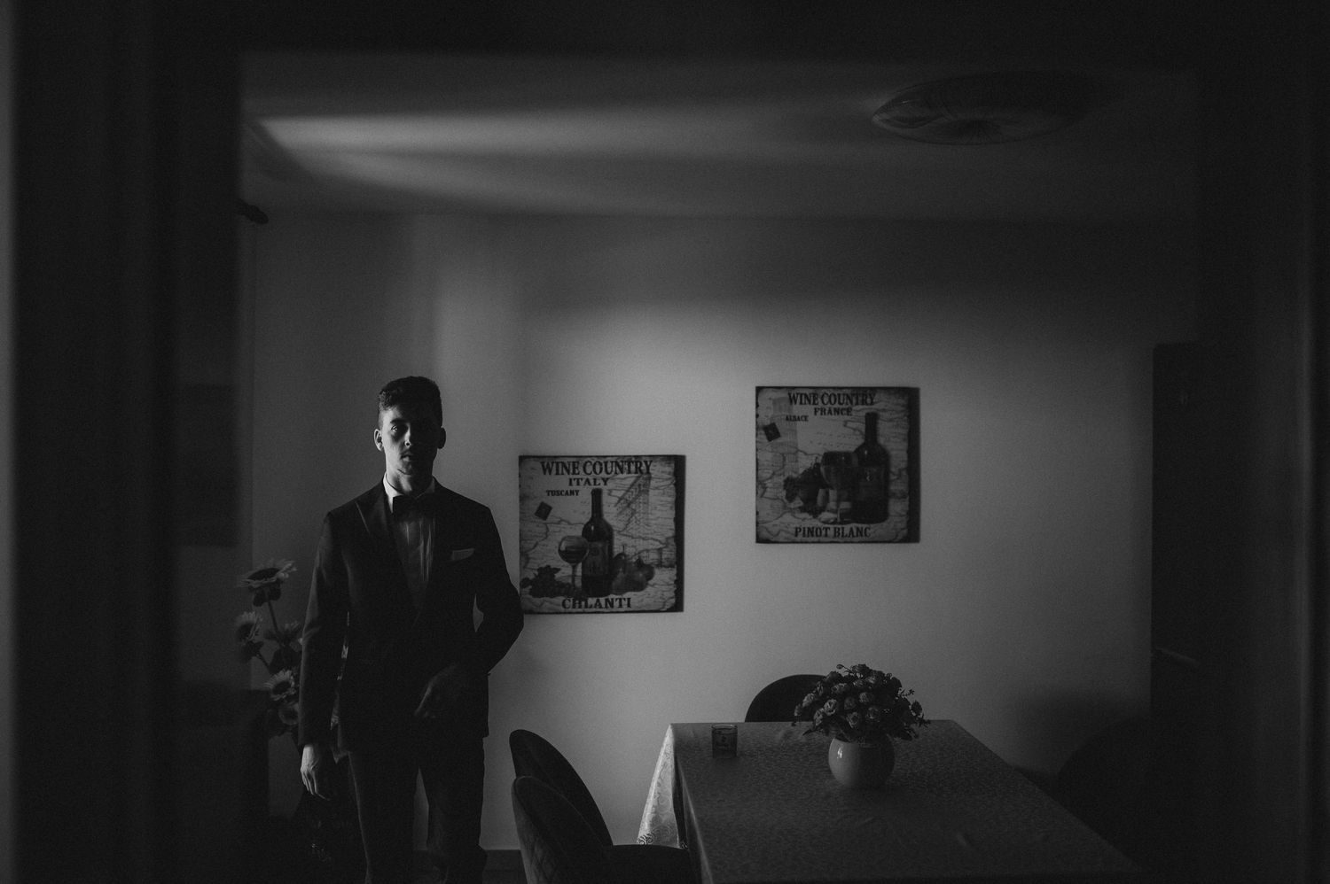 Groom standing alone in dramatic black and white moody wedding preparation photo.