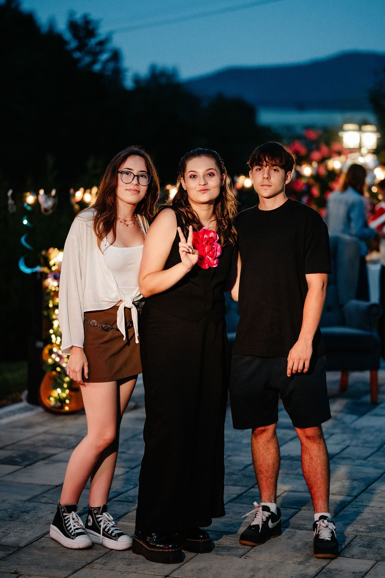 Three teenagers posing together at a beautifully lit outdoor evening celebration party.