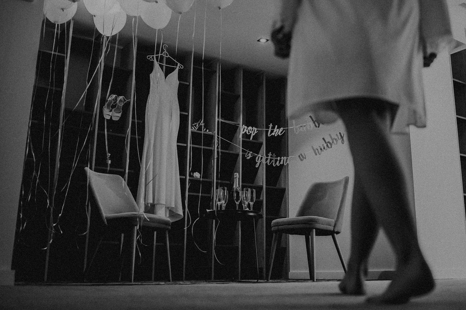 Wedding dress displayed on hanger among balloons and ribbons in black and white photo.