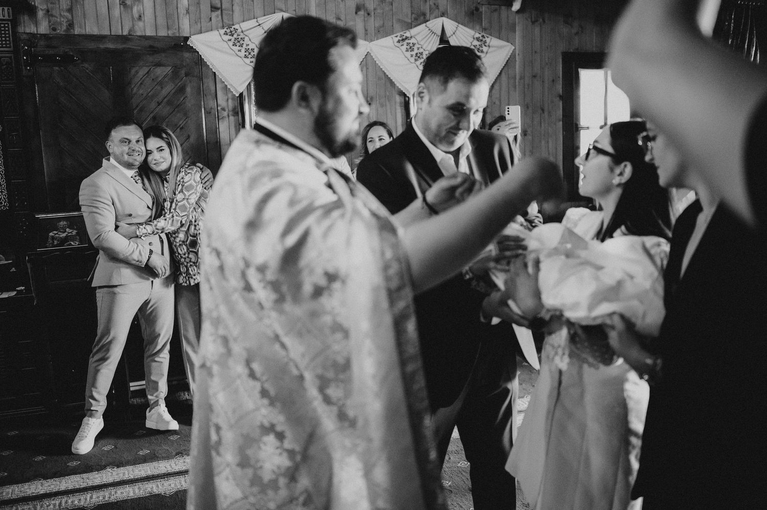 Priest performs Orthodox christening ceremony with godparents and baby in a decorated church.