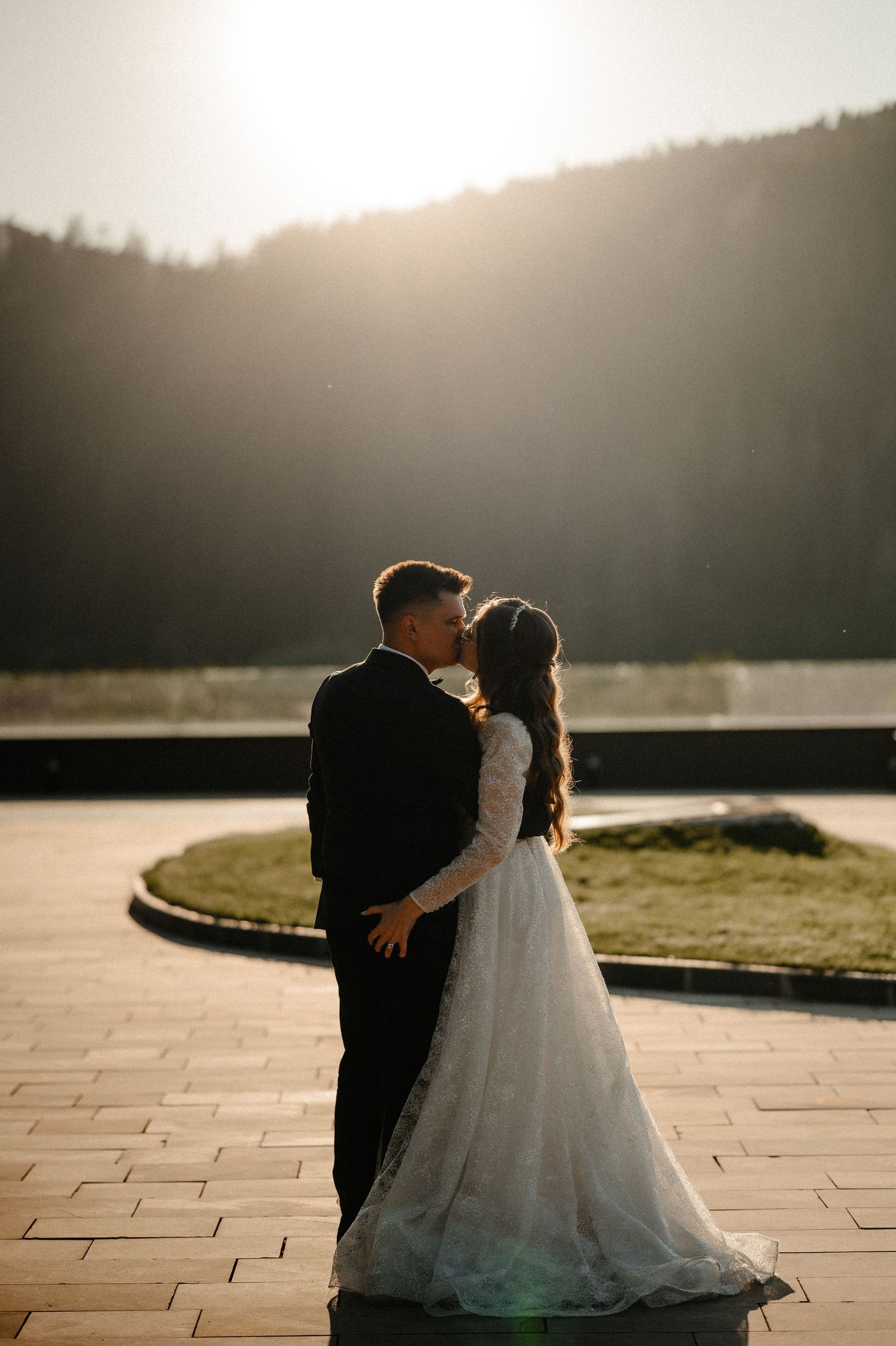 Bride and groom sharing a kiss in golden sunlight with mountain landscape behind them.