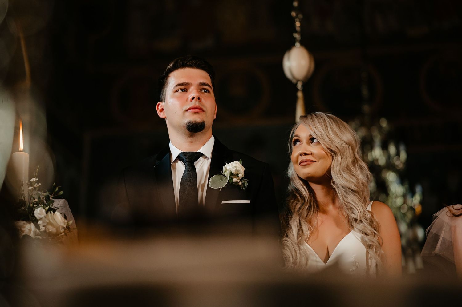 Bride and groom looking upward during candlelit Orthodox wedding ceremony in a historic church.