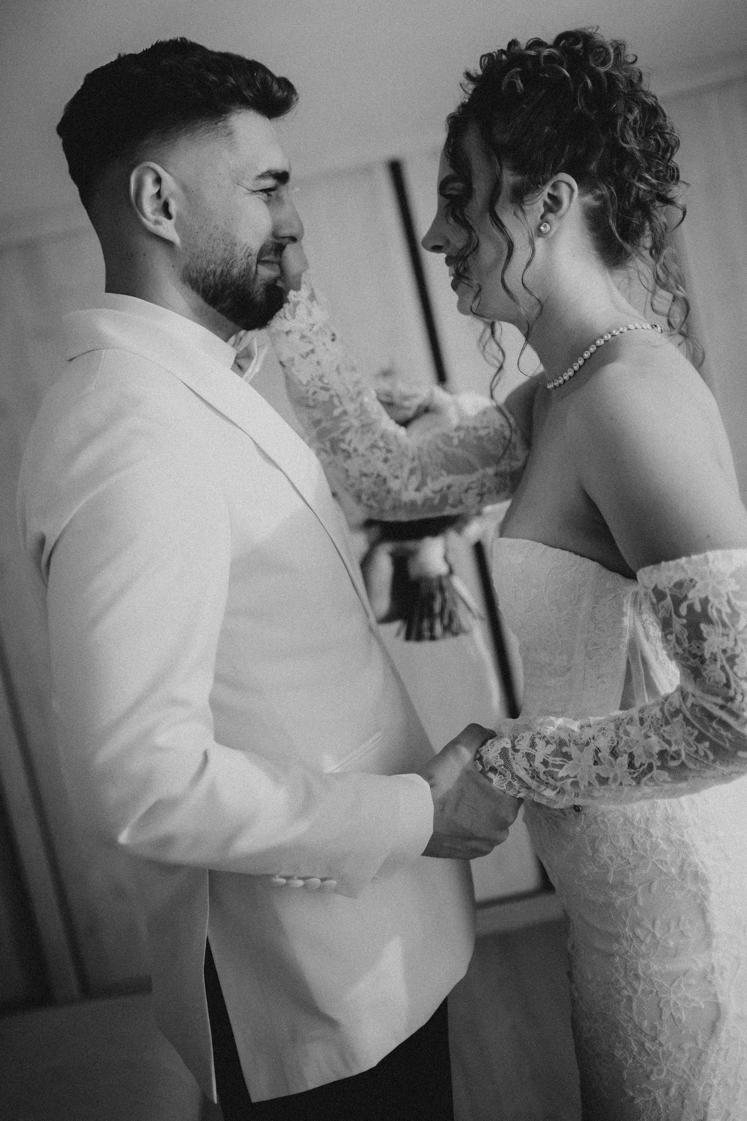 Black and white photo of bride and groom sharing tender moment, holding hands in wedding attire before ceremony.