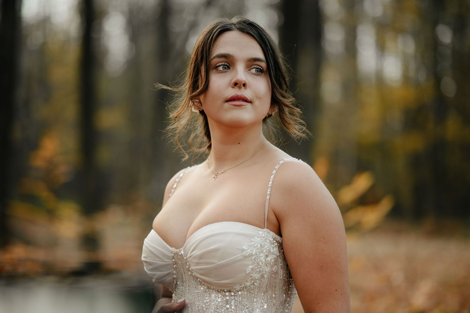 Woman in white bridal gown posing in autumn forest with golden foliage background.