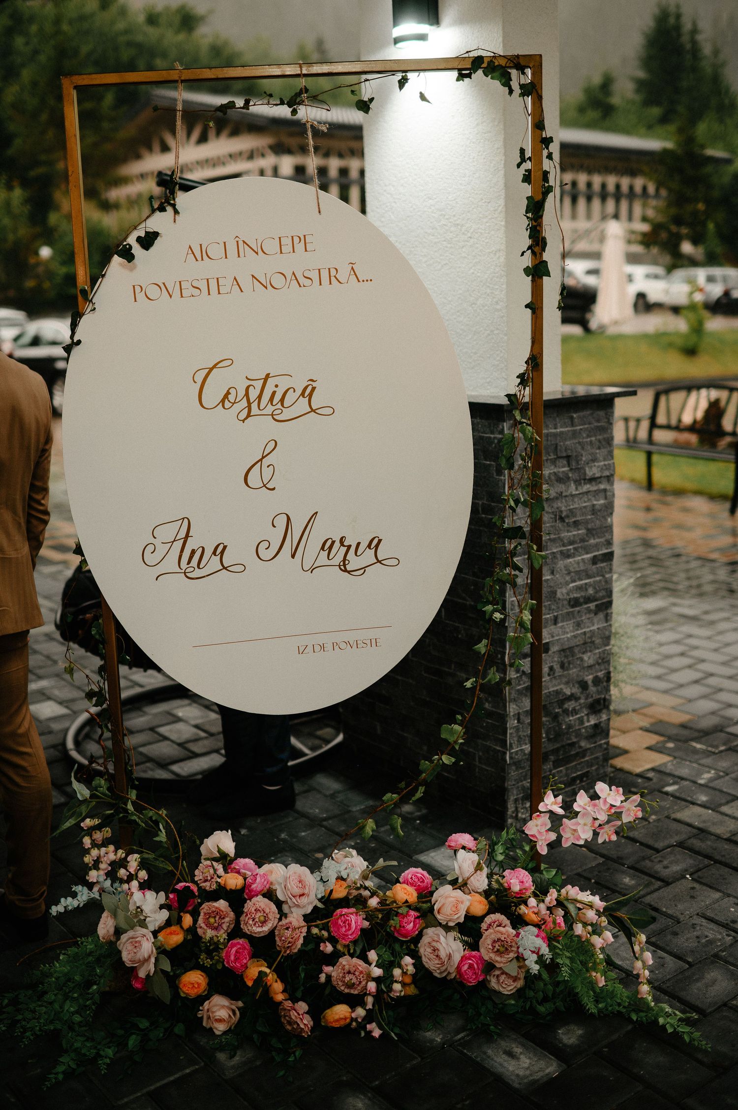Wedding welcome sign for Costica and Ana Maria with pink floral arrangement on cobblestone.