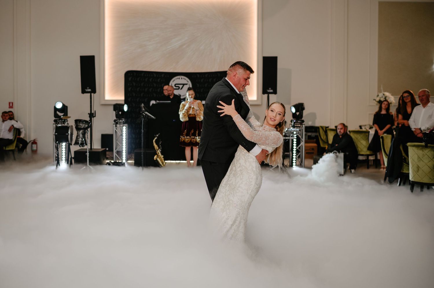 Bride and groom share romantic first dance on fog-covered dance floor at wedding reception.