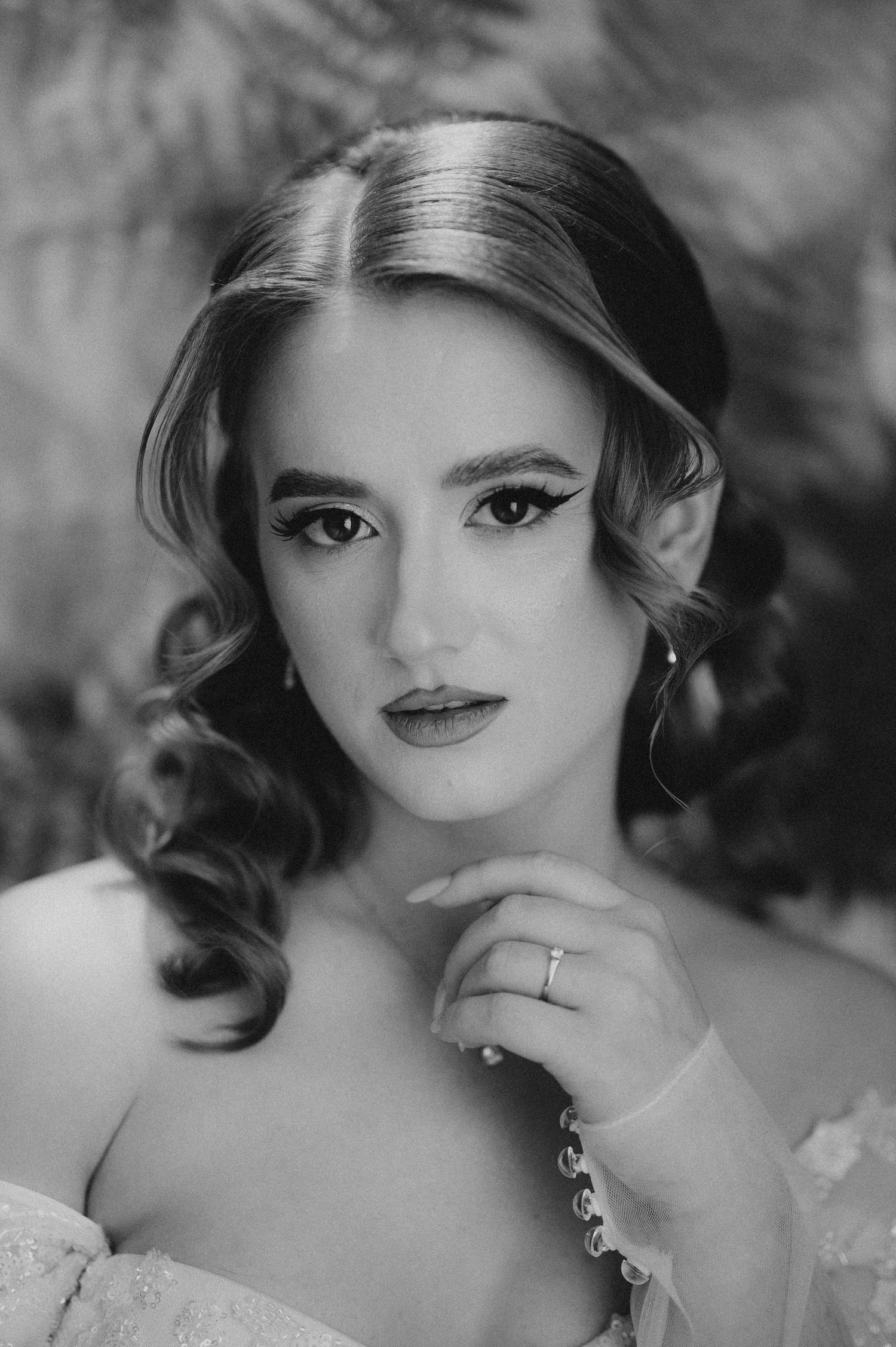 Black and white bridal portrait of a young woman with elegant curled hair, wearing a ring and delicate jewelry.